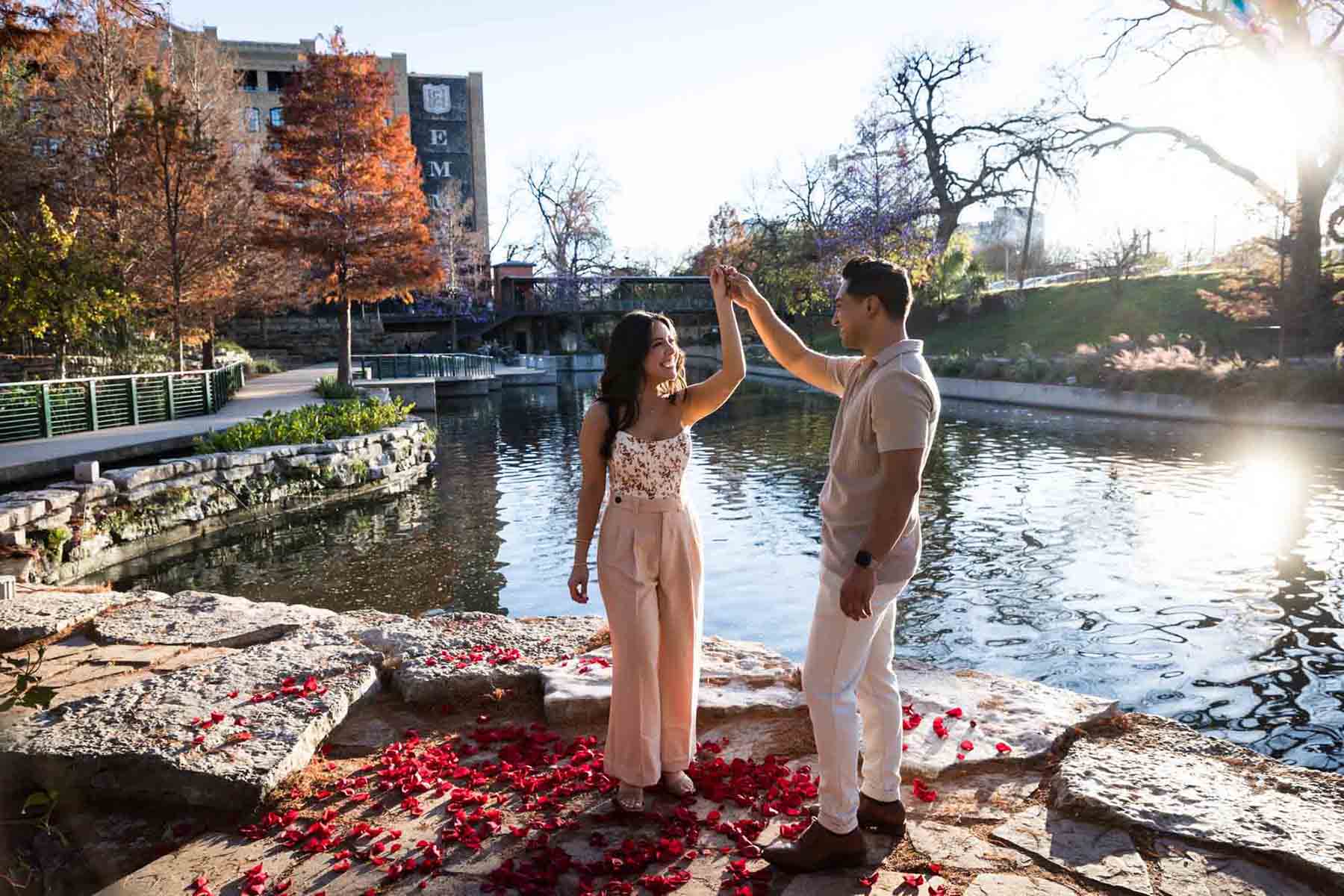 Man holding woman's hand in the air with rose petals at his feet and Riverwalk in the background