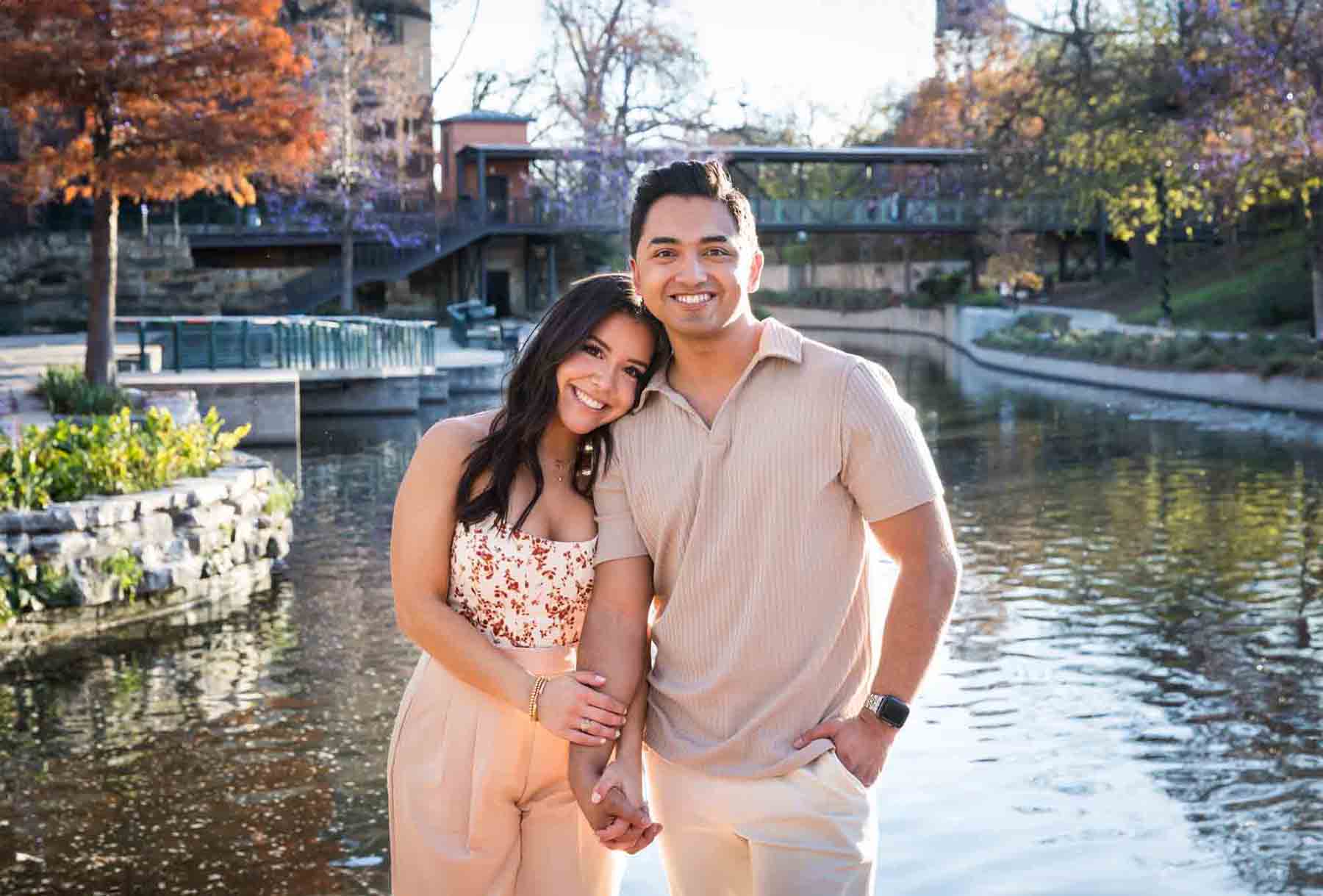 Couple holding hands and smiling into camera with Riverwalk in the background