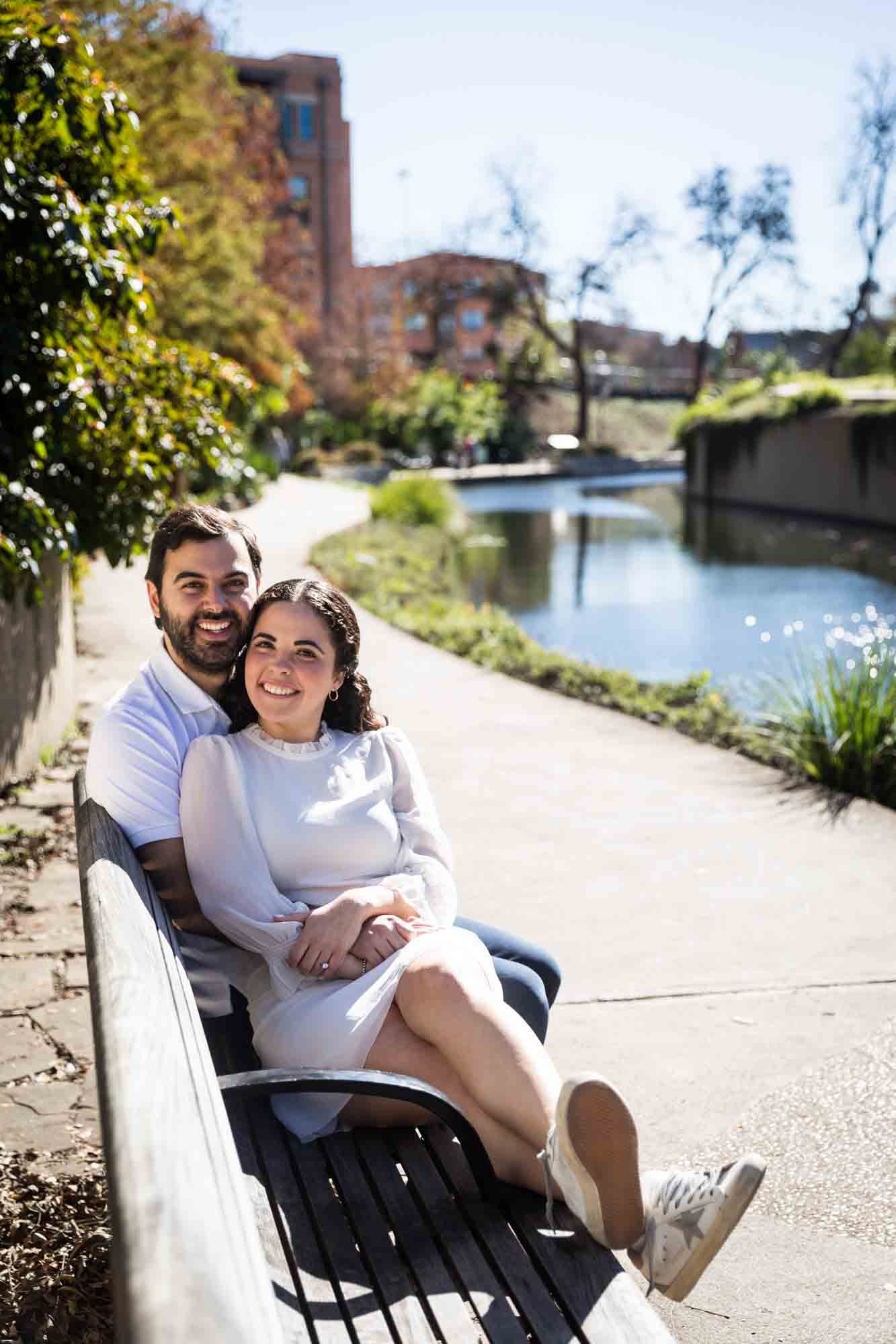 Couple hugging on bench by Riverwalk by San Antonio photographer, Kelly Williams