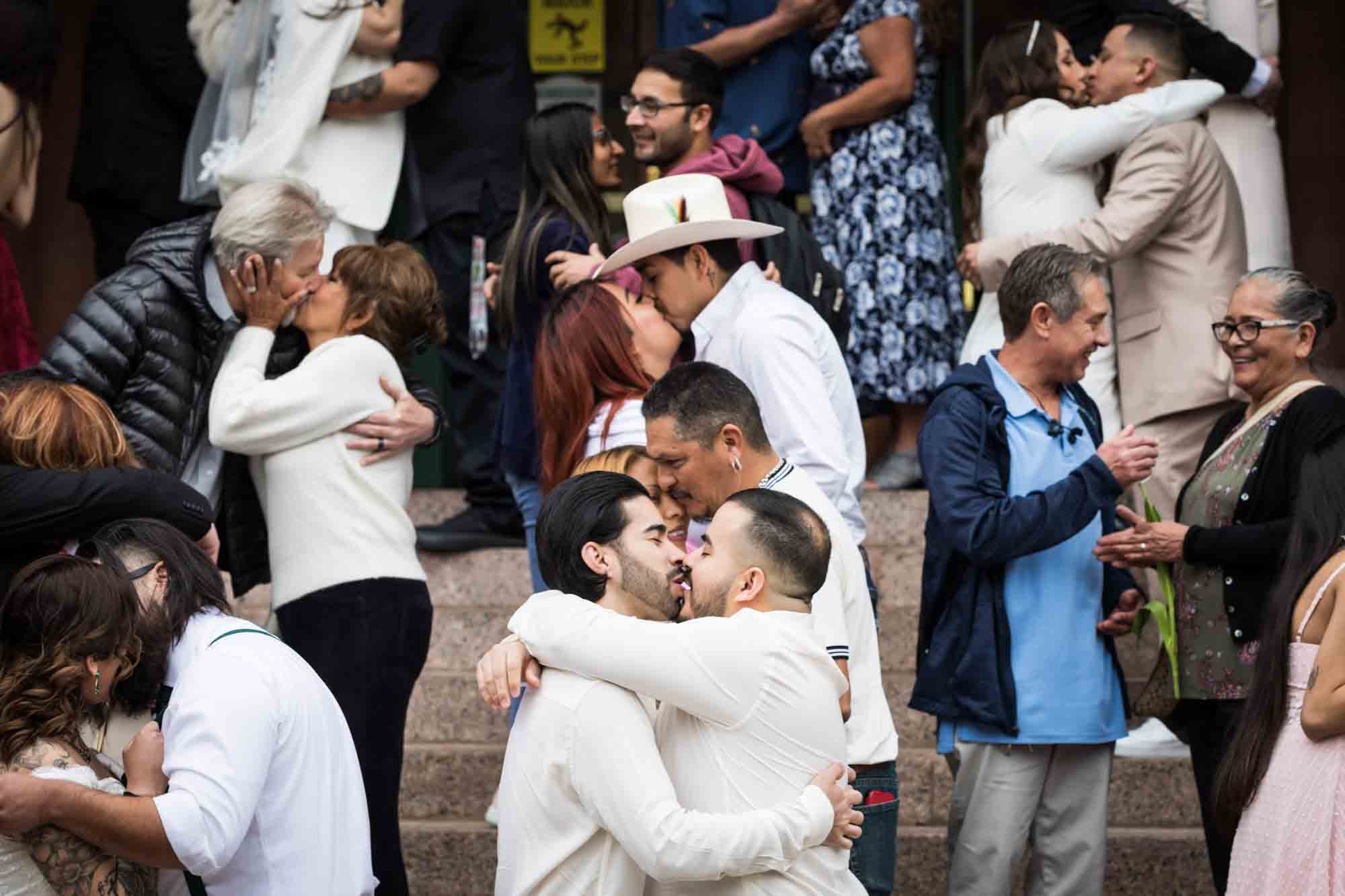 Crowd of bride and grooms kissing in front of courthouse steps at night for an article on the Bexar county mass wedding event