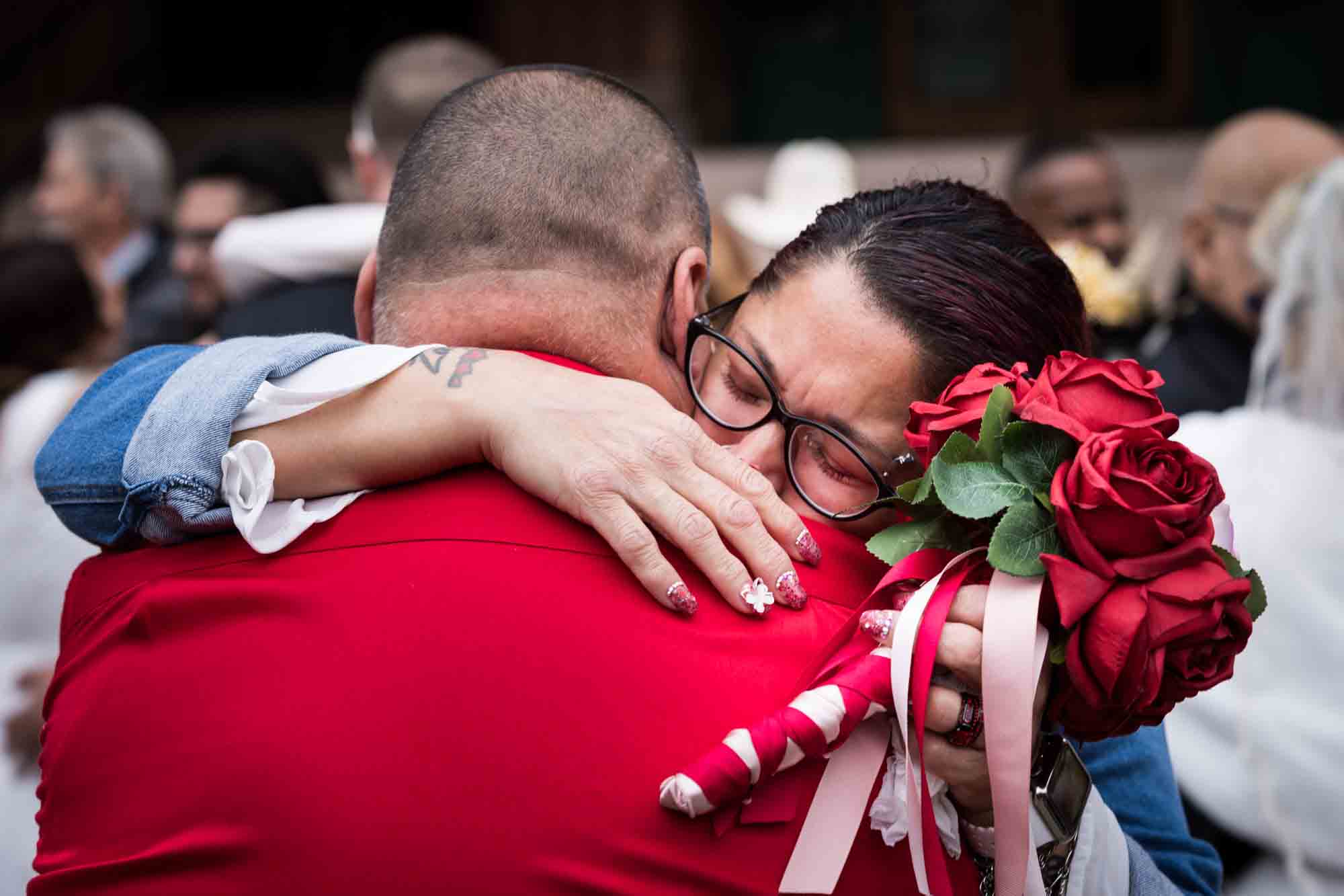 Woman with red flower bouquet crying and holding onto groom wearing red shirt for an article on the Bexar county mass wedding event