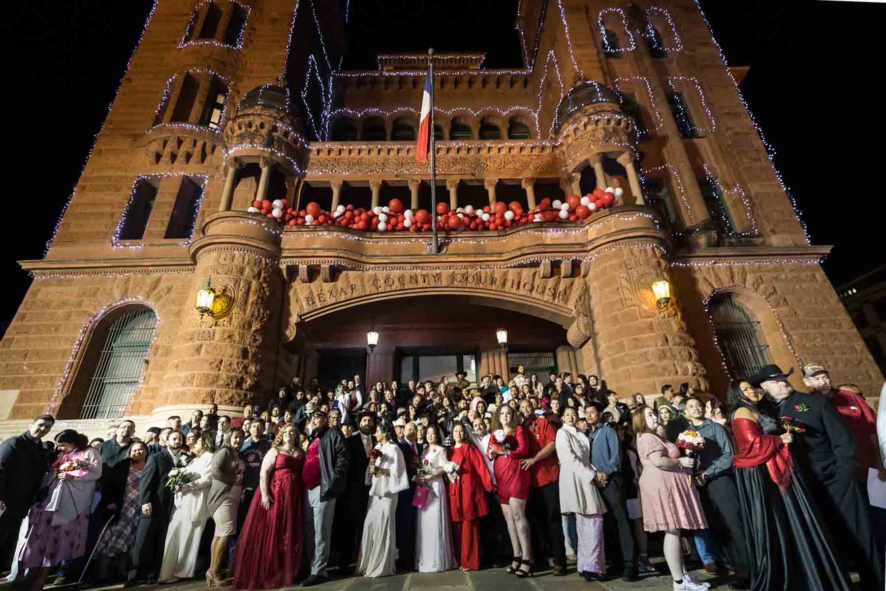 Couples standing in front of the Bexar County Courthouse at night for an article on the Bexar county mass wedding event
