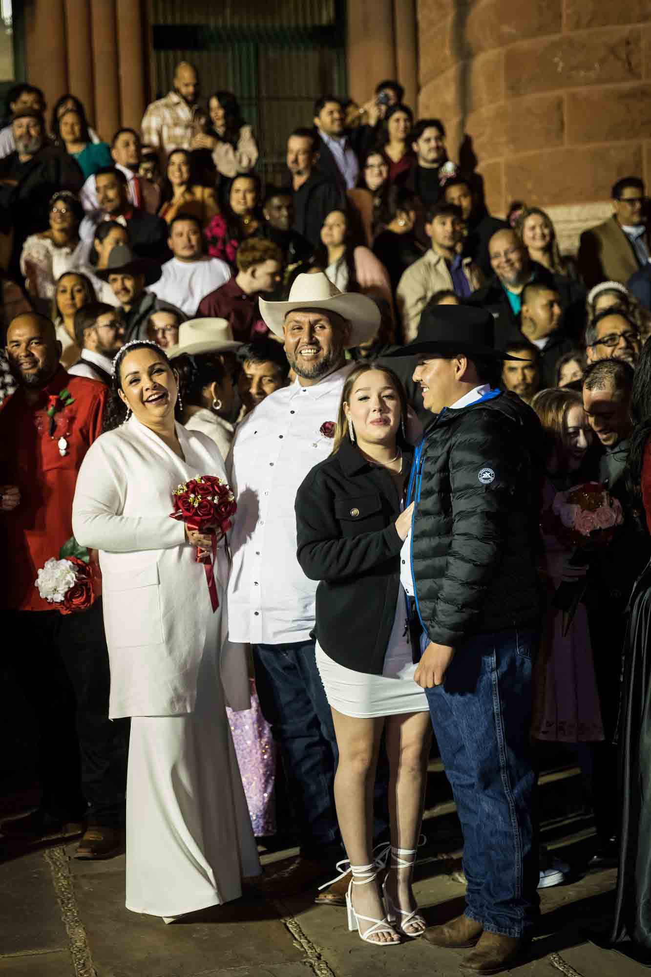 Crowd of bride and grooms standing in front of courthouse steps at night for an article on the Bexar county mass wedding event
