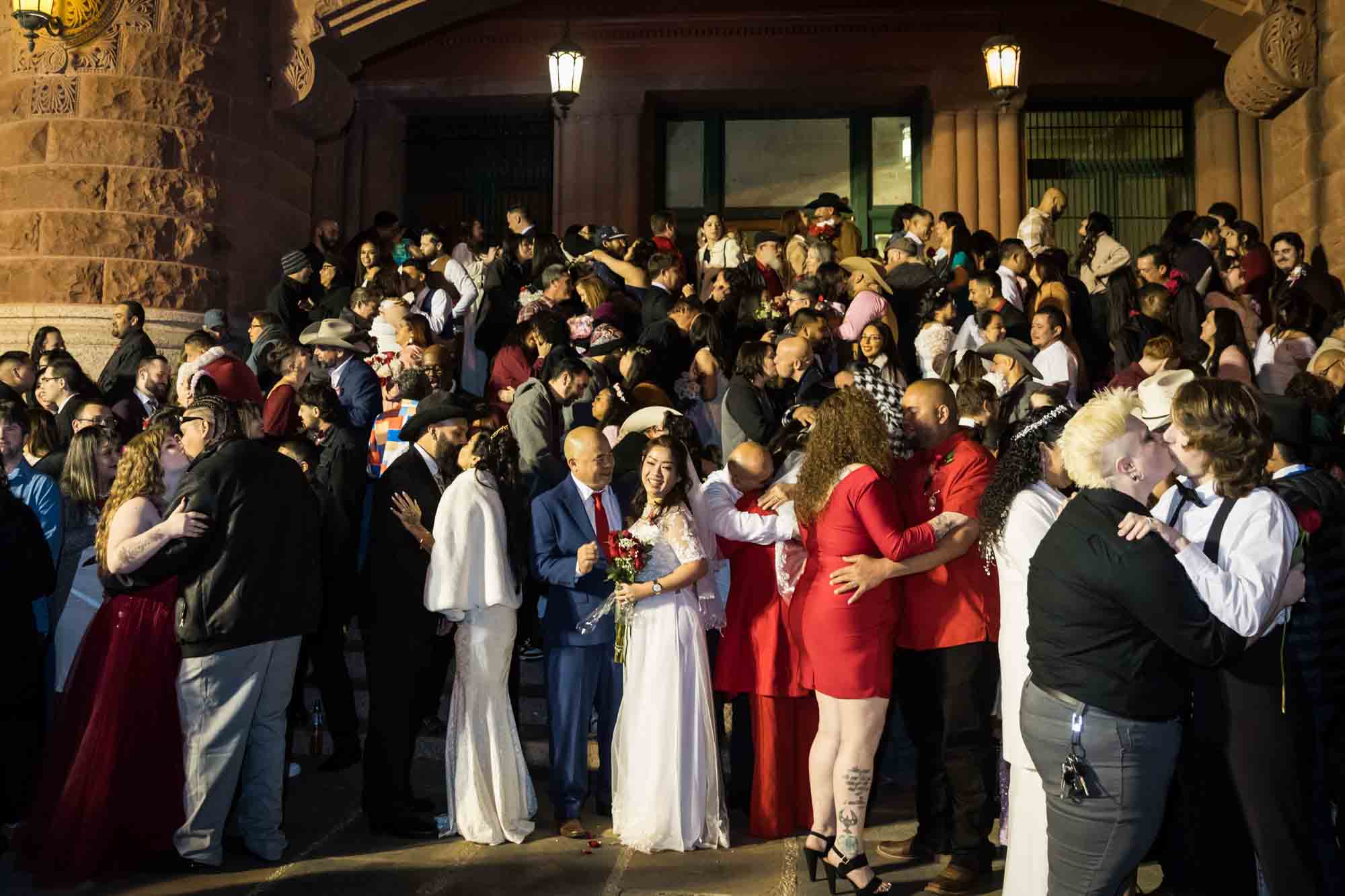 Crowd of bride and grooms standing in front of courthouse steps at night for an article on the Bexar county mass wedding event