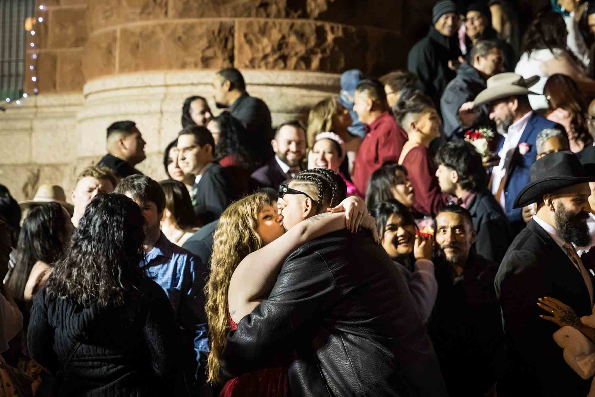 Crowd of bride and grooms kissing in front of courthouse steps at night for an article on the Bexar county mass wedding event