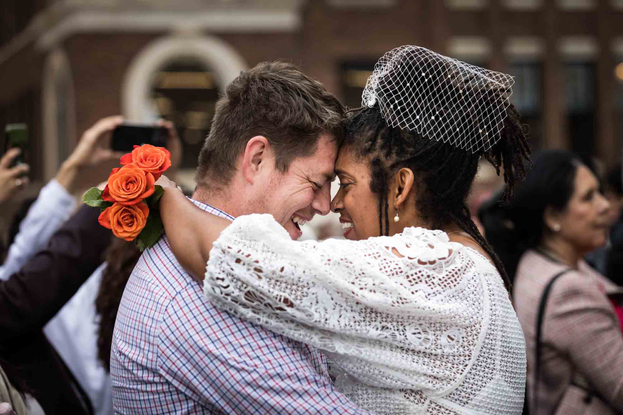 Bride wearing veil hat hugging groom and holding orange flowers for an article on the Bexar county mass wedding event