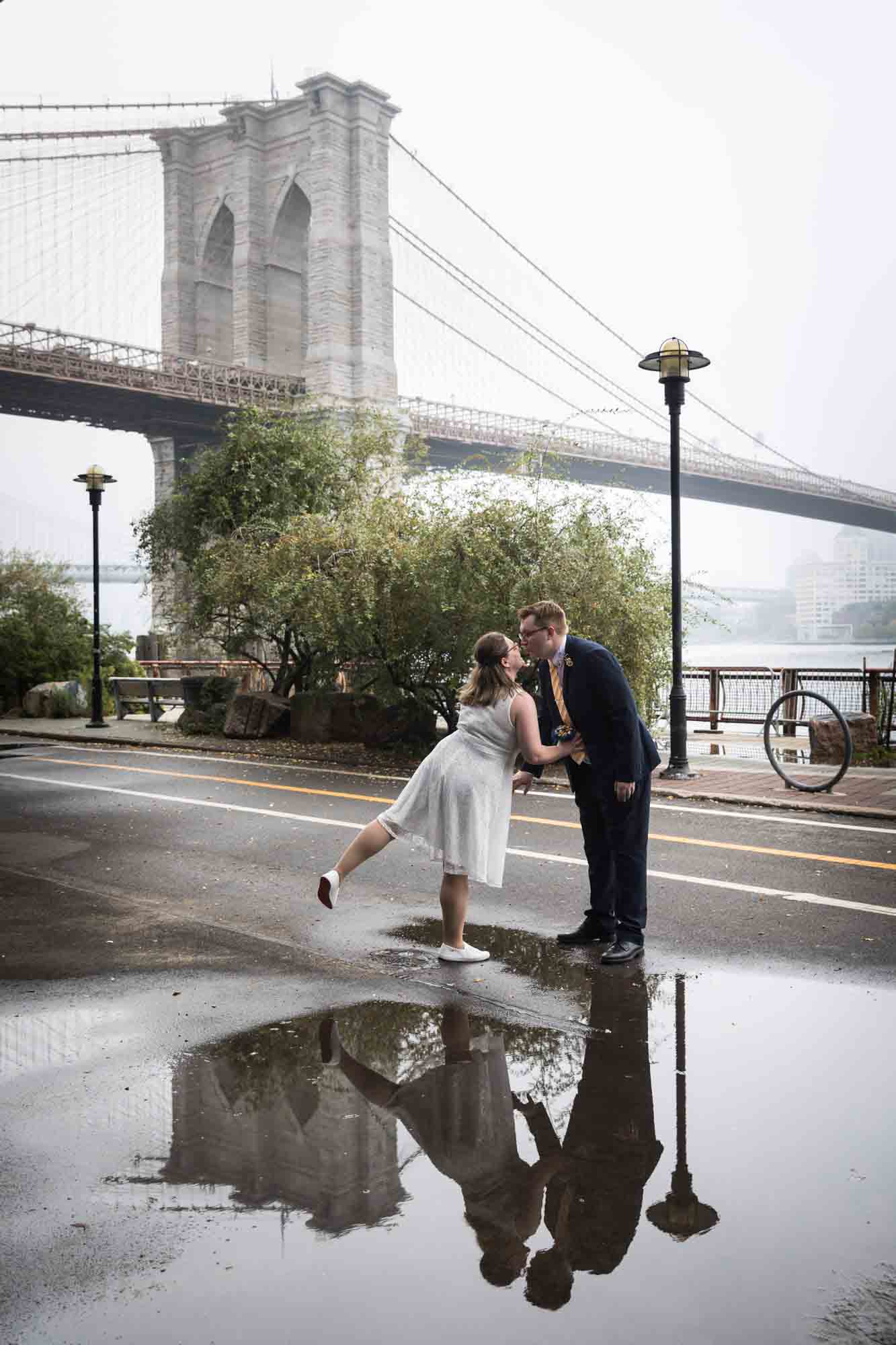 Couple about to kiss in front of rain puddle and Brooklyn Bridge in background for an article on how to get a marriage license in San Antonio