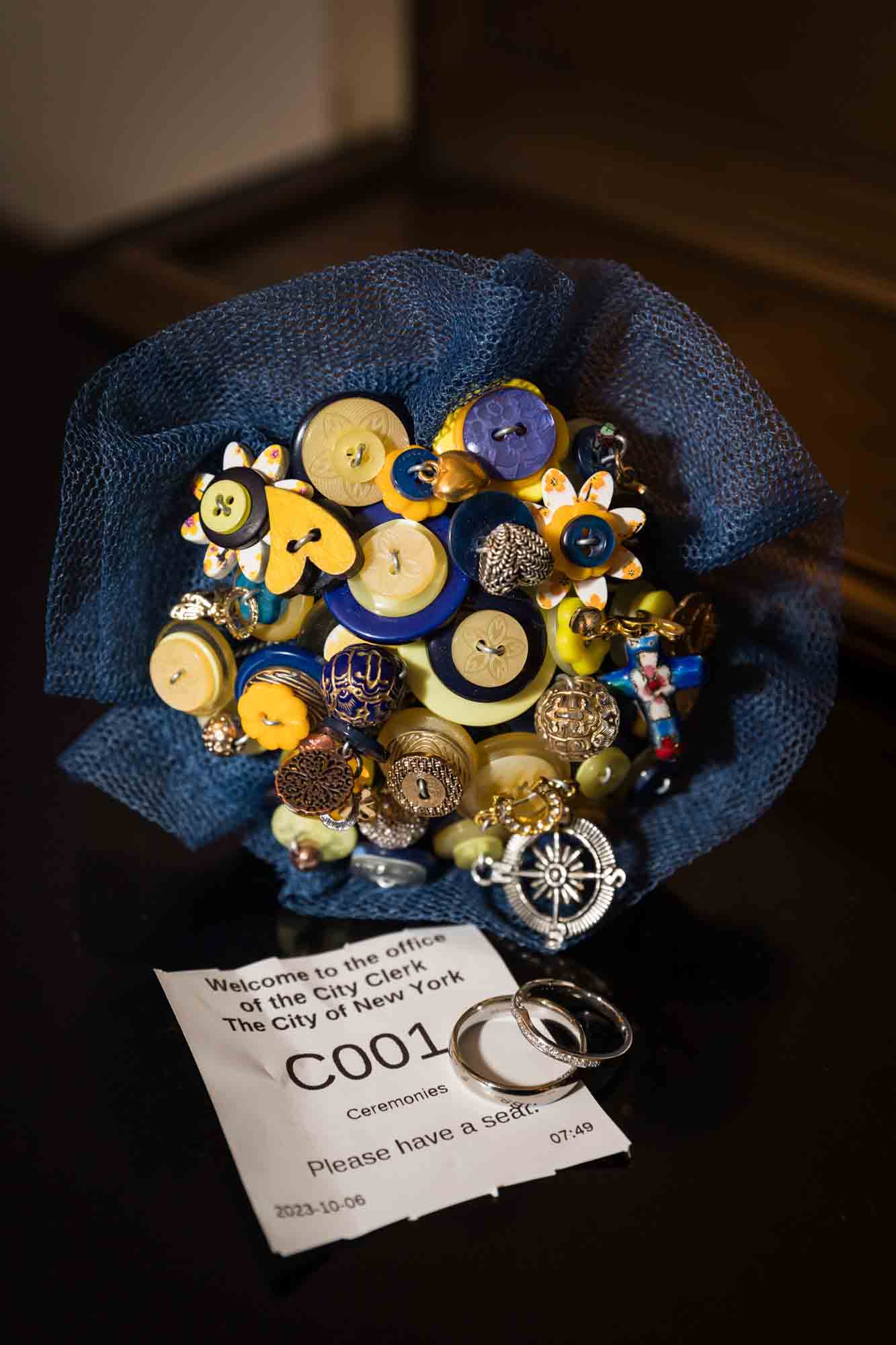 Button bouquet with blue tulle surrounding it, wedding rings, and strip of paper with numbers for an article on how to get a marriage license in San Antonio