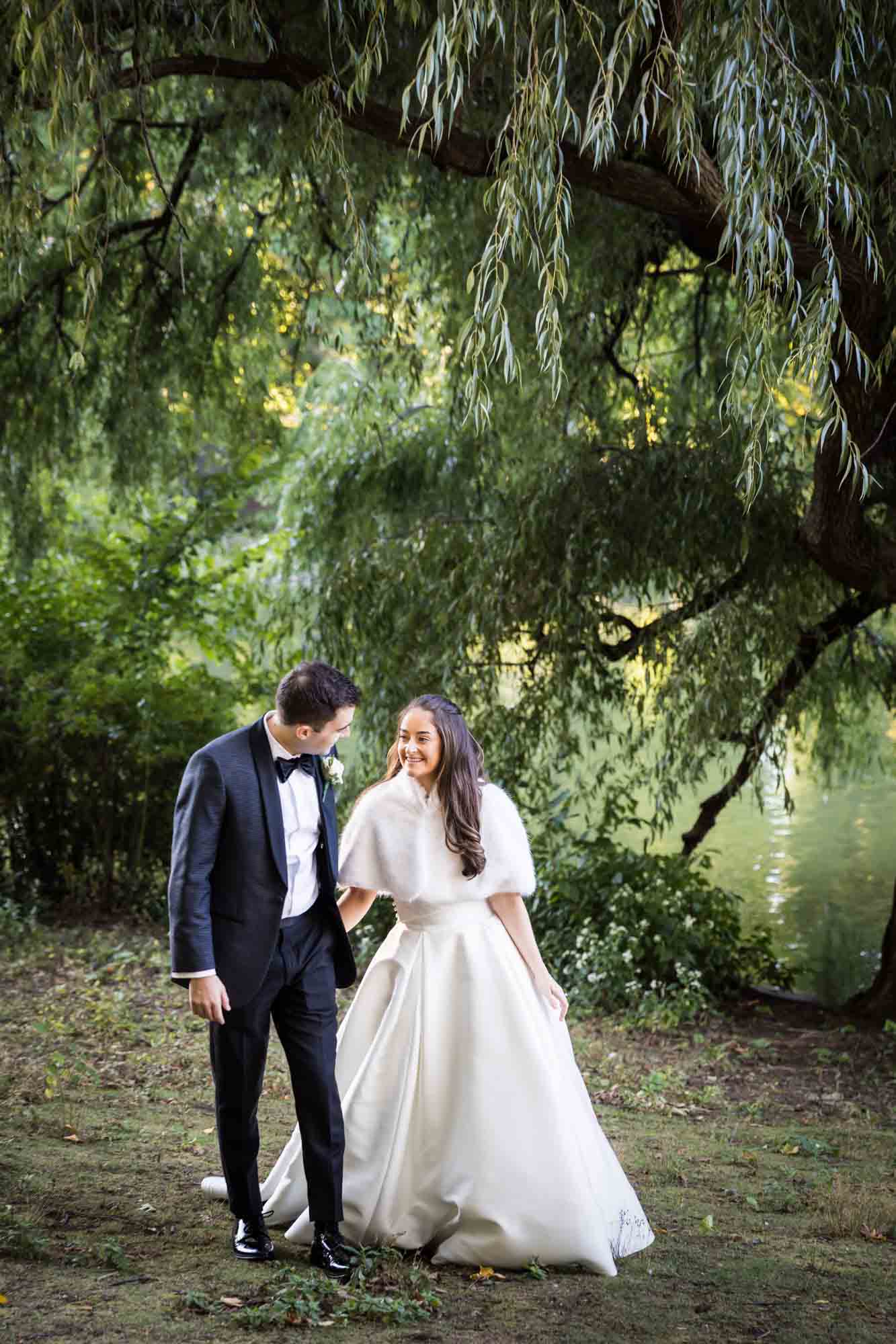 Bride and groom holding hands and walking in front of willow trees