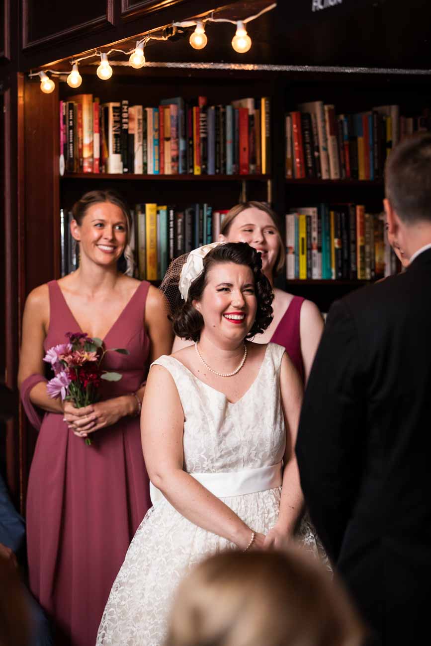 Bride smiling in front of bridal party and bookcase for an article on how to become a wedding officiant in San Antonio