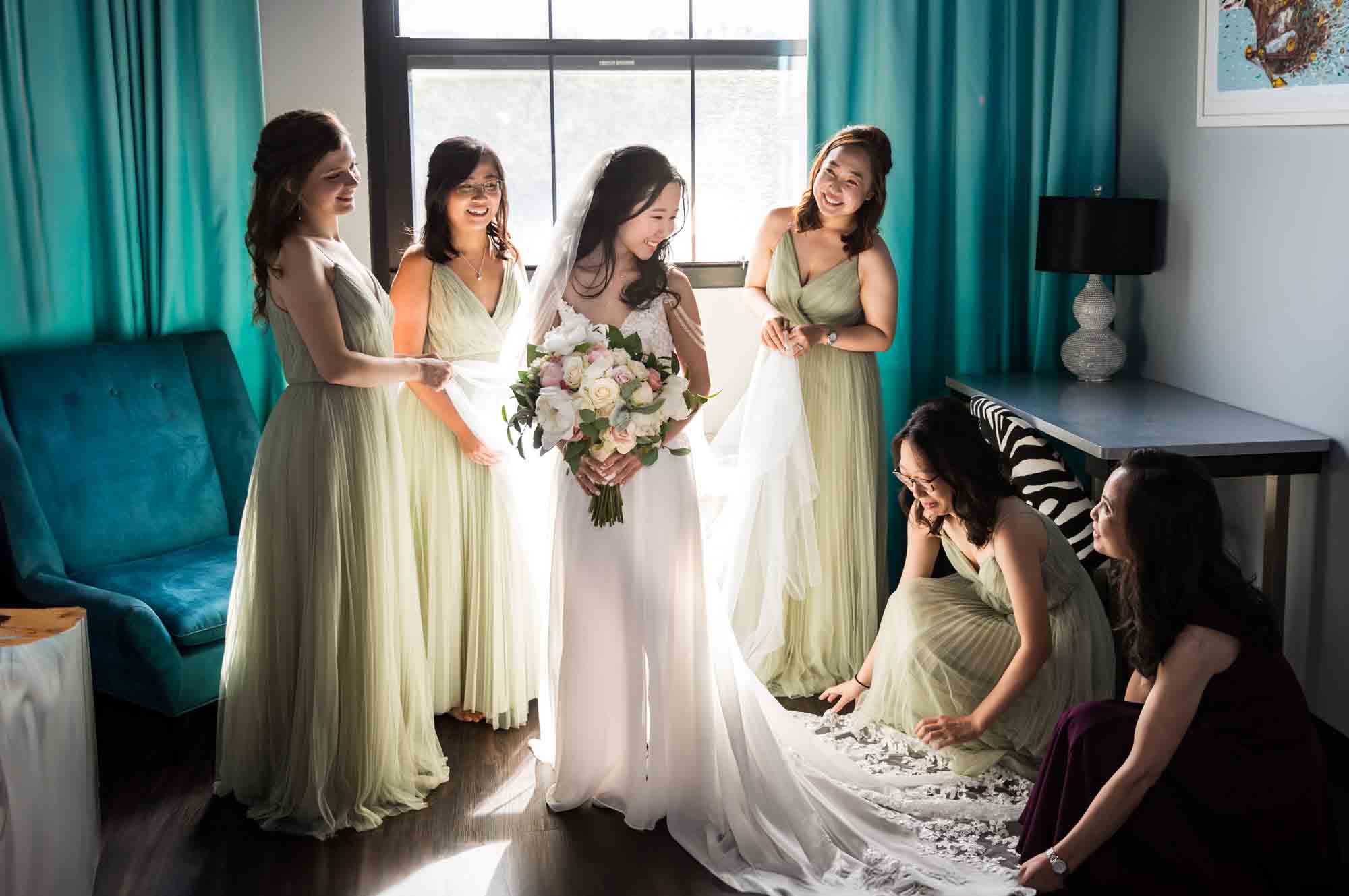 Bridesmaids helping bride with veil in front of window