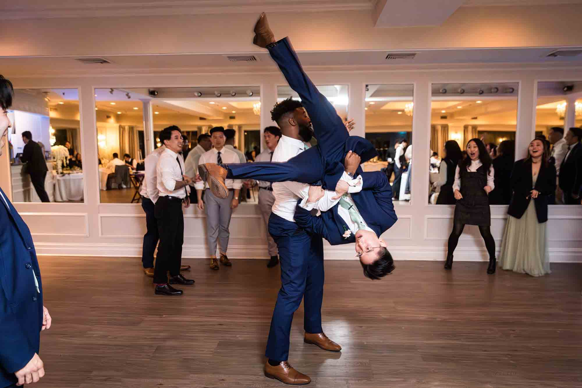 Man flipping groom upside down on dance floor for an article on should you give your wedding photographer a shot list