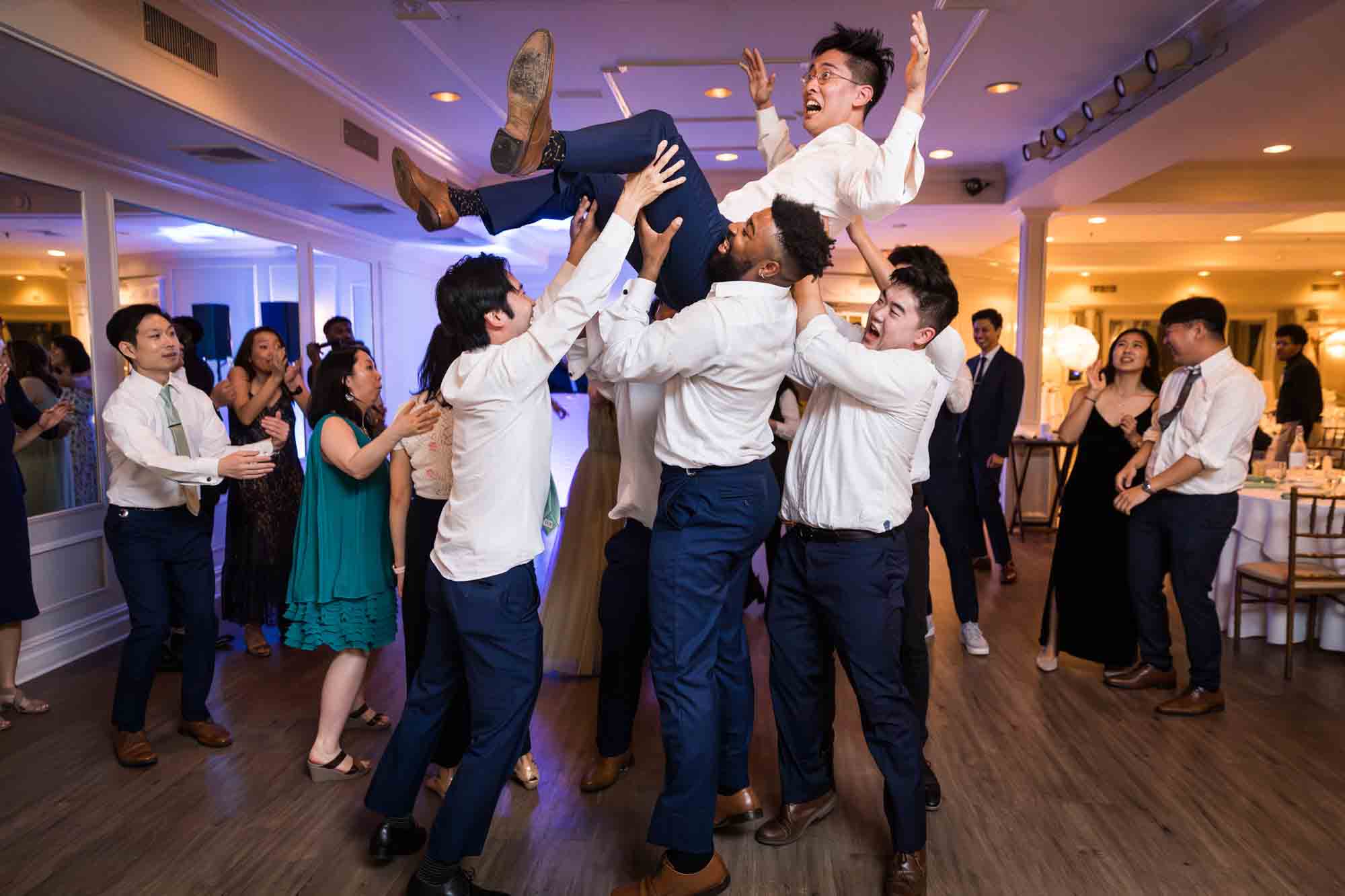Guests throwing groom into the air at reception for an article on should you give your wedding photographer a shot list