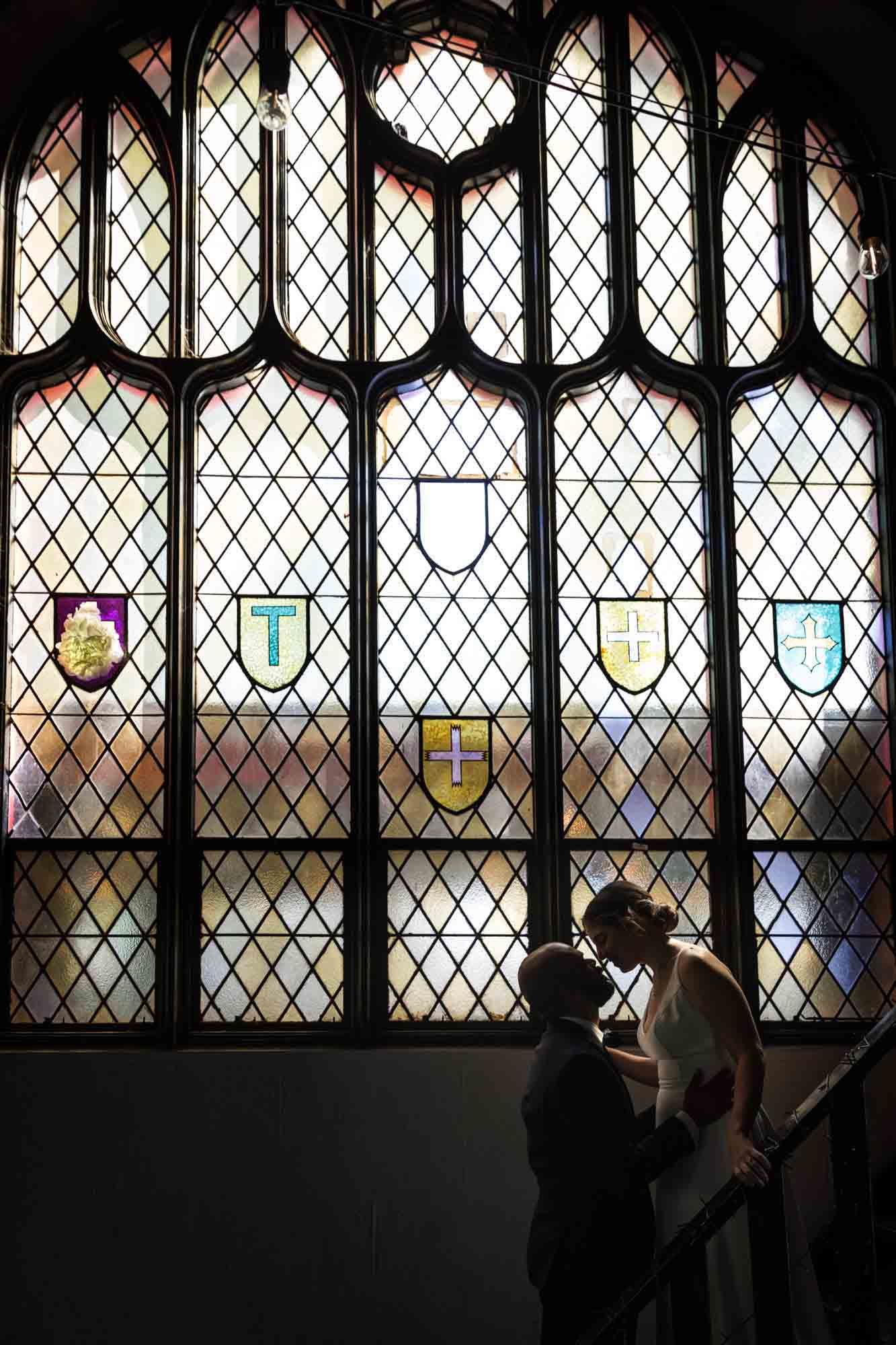 Backlit photo of bride and groom kissing in front of stained glass window