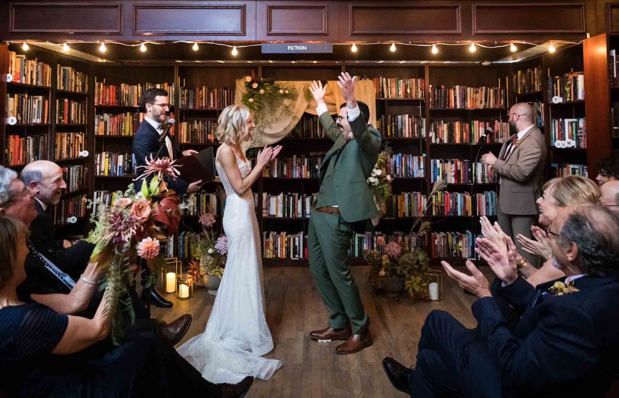 Bride and groom celebrating in front of bookshelf for an article on should you give your wedding photographer a shot list