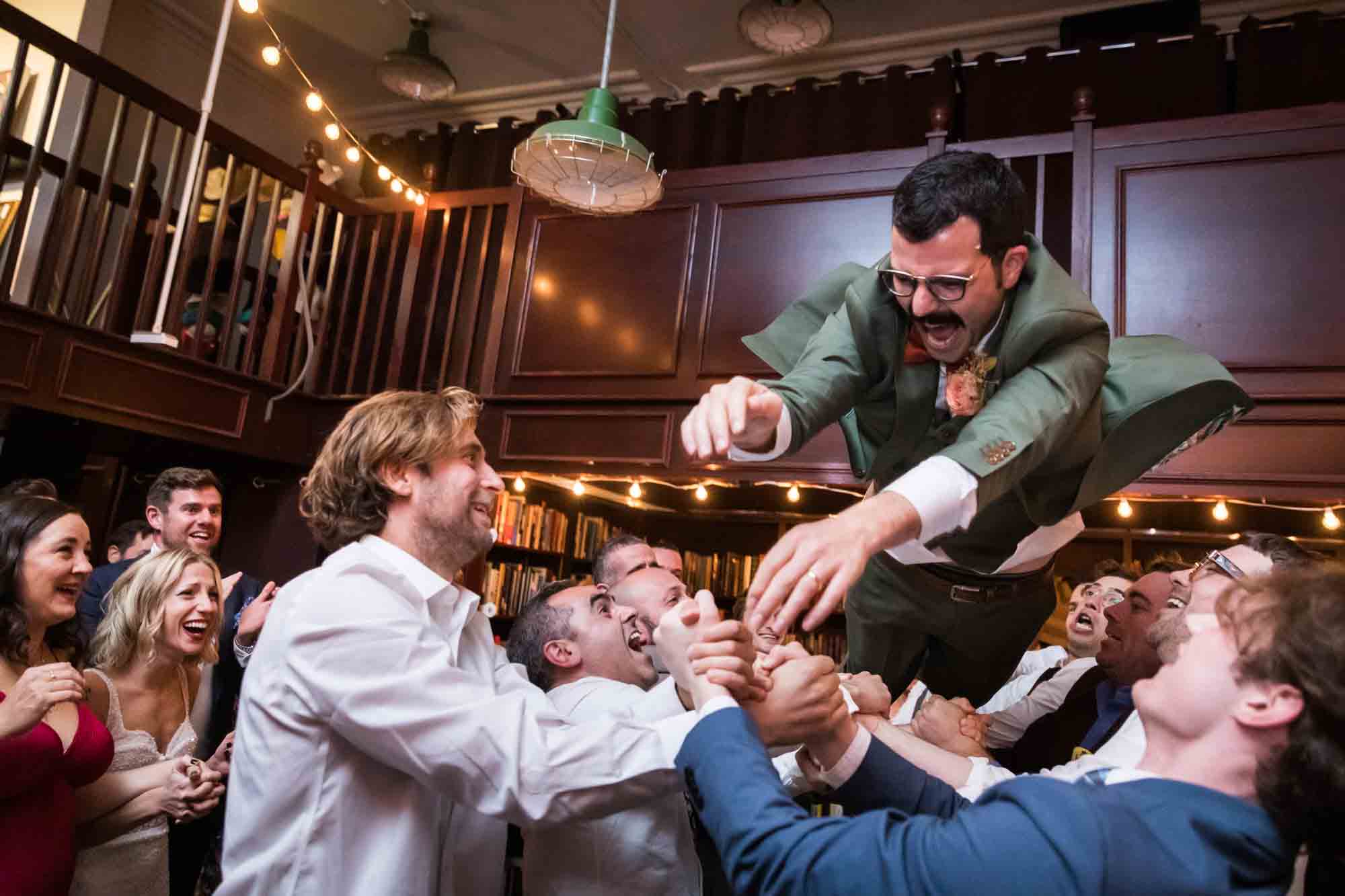Groom getting thrown in the air by guests for an article on should you give your wedding photographer a shot list