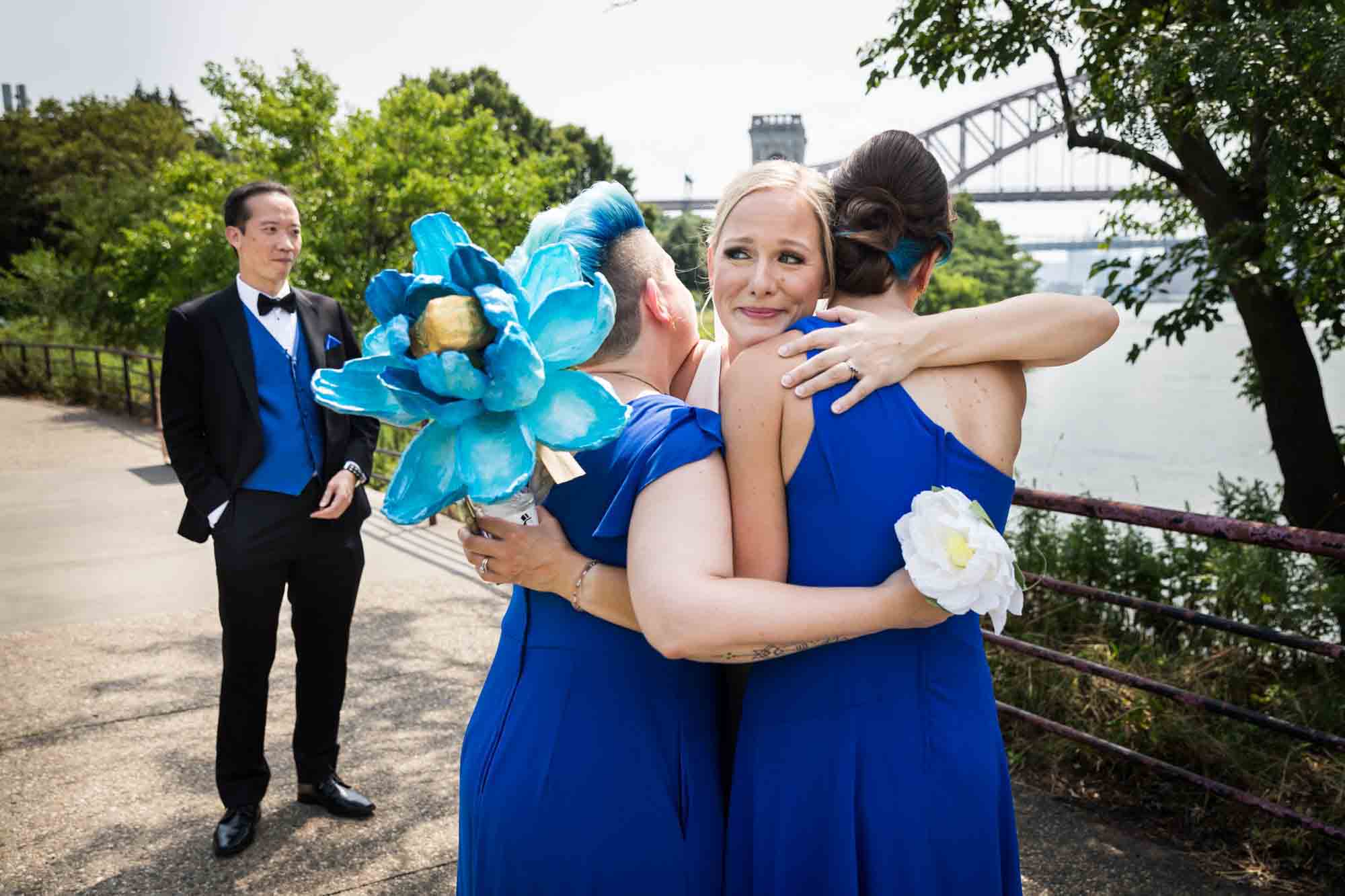 Bride hugging bridesmaids with groom in background