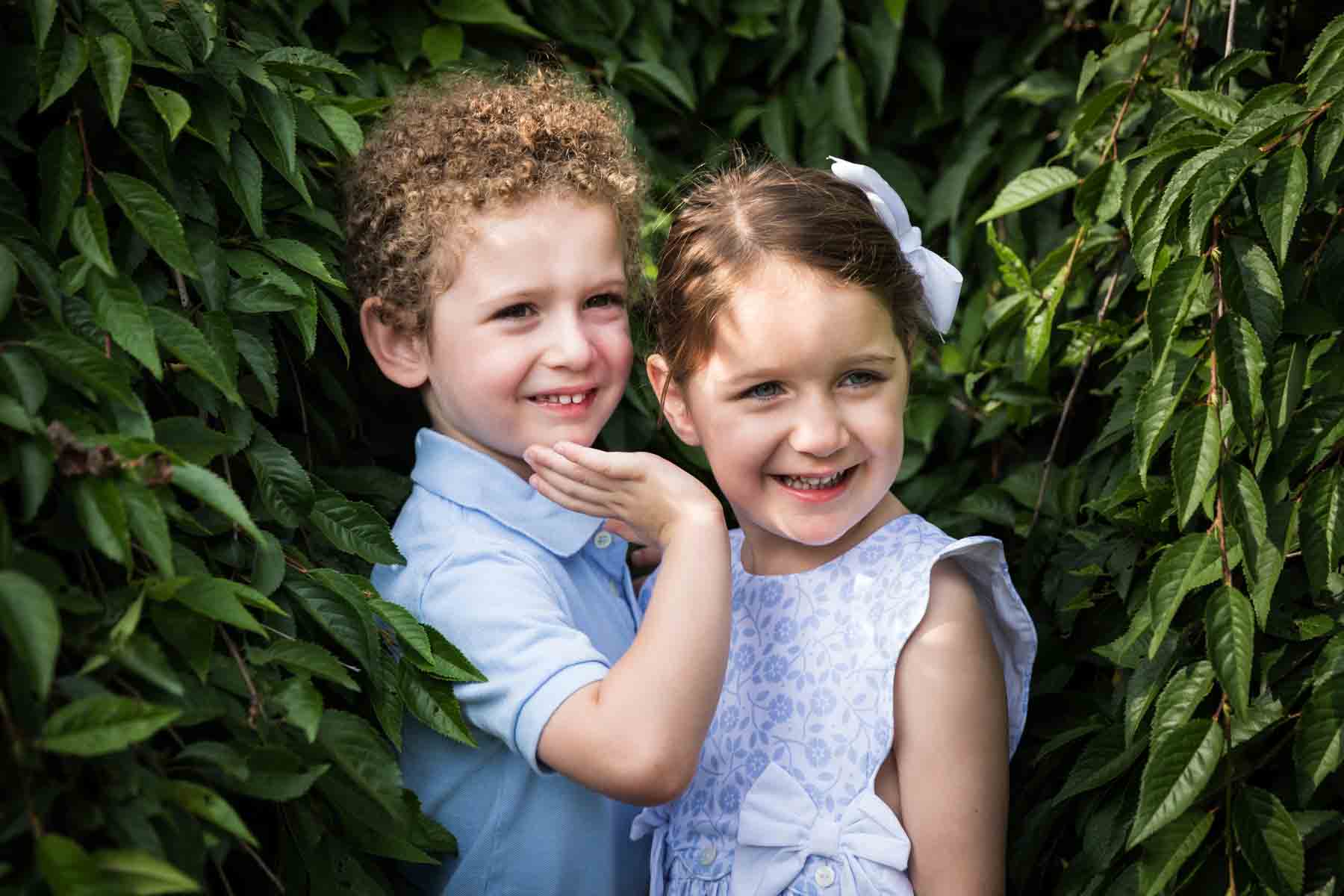Little boy and girl smiling in front of green bush for an article on the best San Antonio parks for family portraits