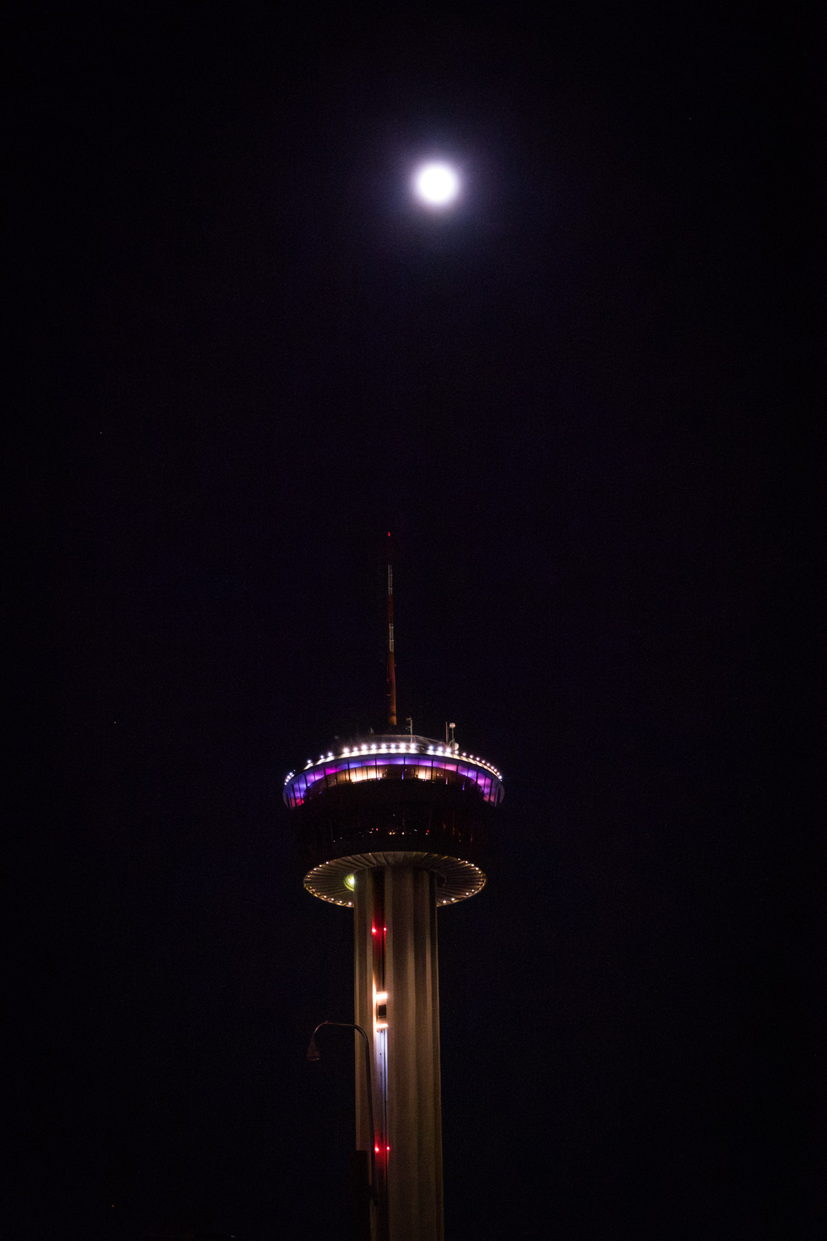 Tower of the Americas at night with a full moon in background for an article on how to propose at the Tower of the Americas