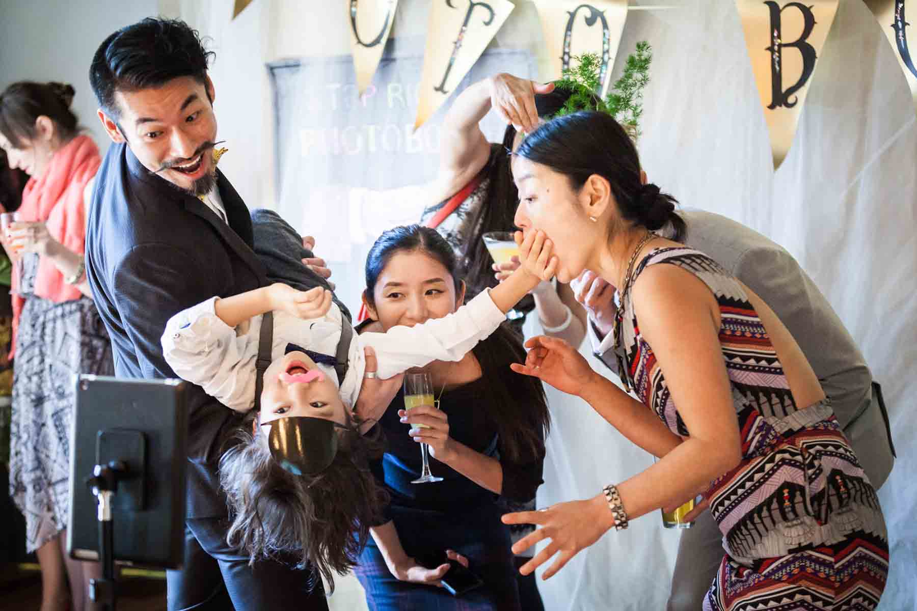 Guests holding up little boy and having fun in front of camera for an article on the best wedding jobs for family and friends