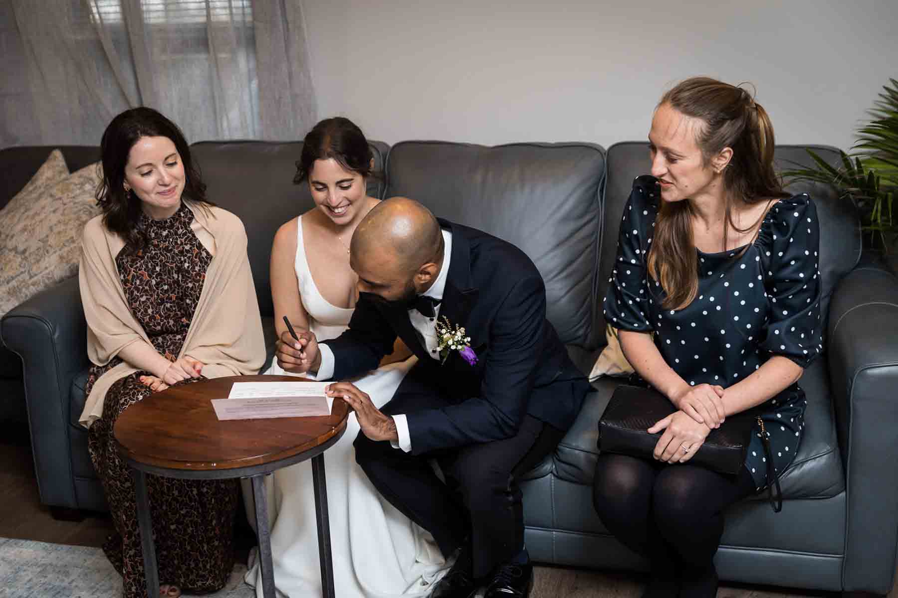 Groom signing marriage license surrounded by three women for an article on the best wedding jobs for family and friends