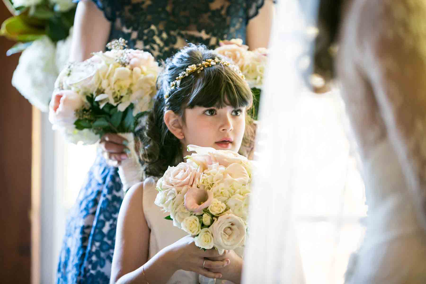 Little flower girl holding flower bouquet behind bride for an article on the best wedding jobs for family and friends