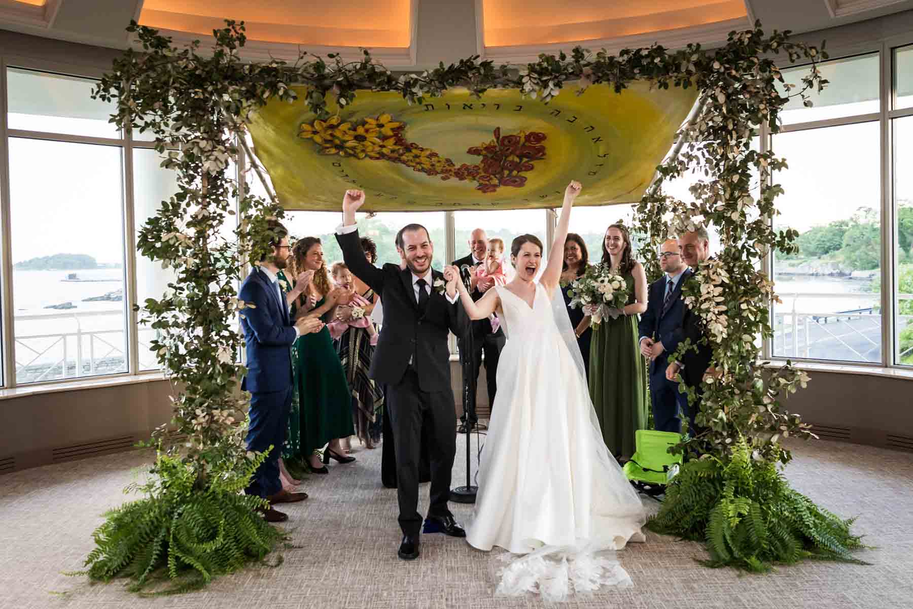 Bride and groom cheering in front of chuppah and family for an article on the best wedding jobs for family and friends
