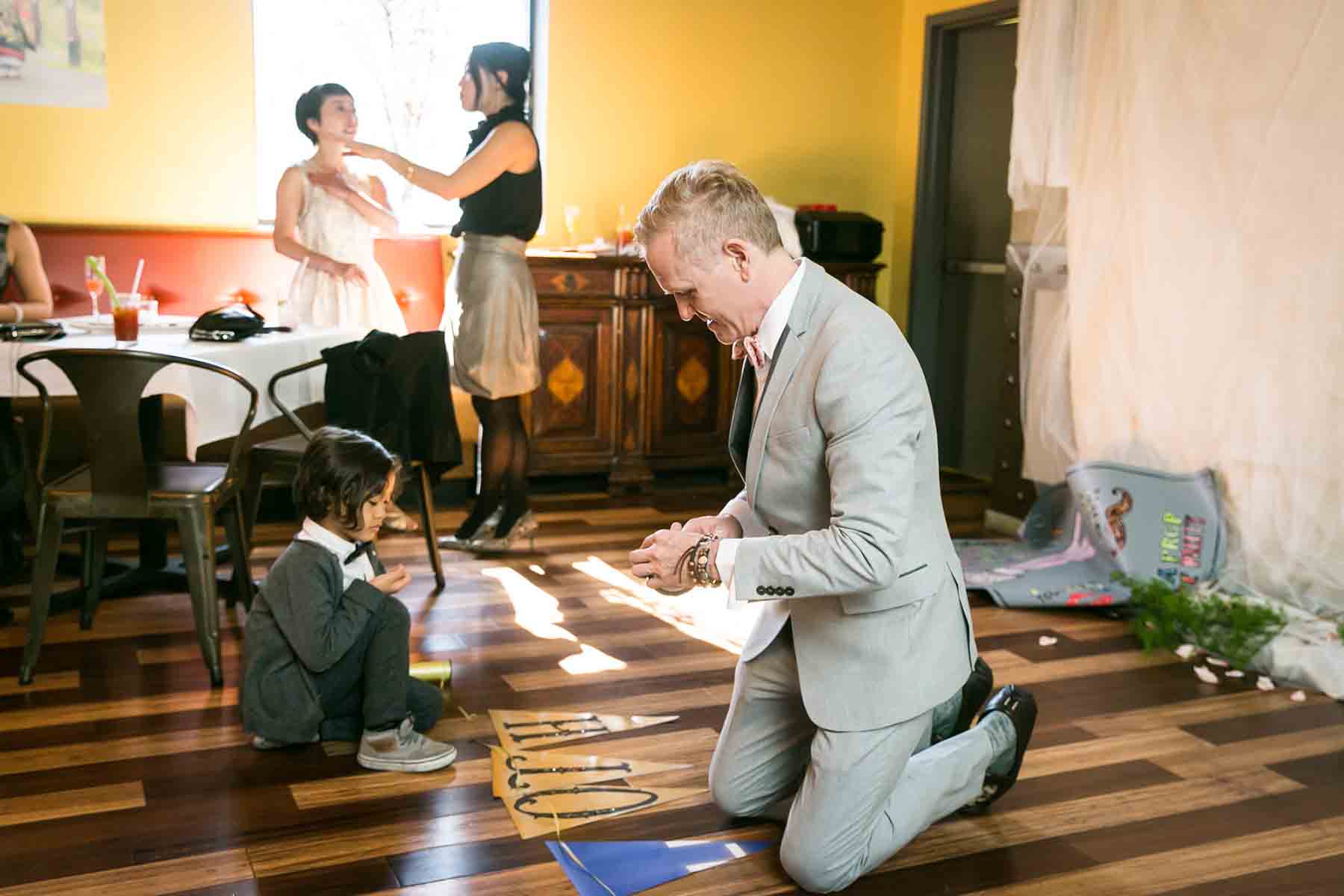 Man kneeling on floor with little boy trying to put together a wedding decorative banner for an article on the best wedding jobs for family and friends