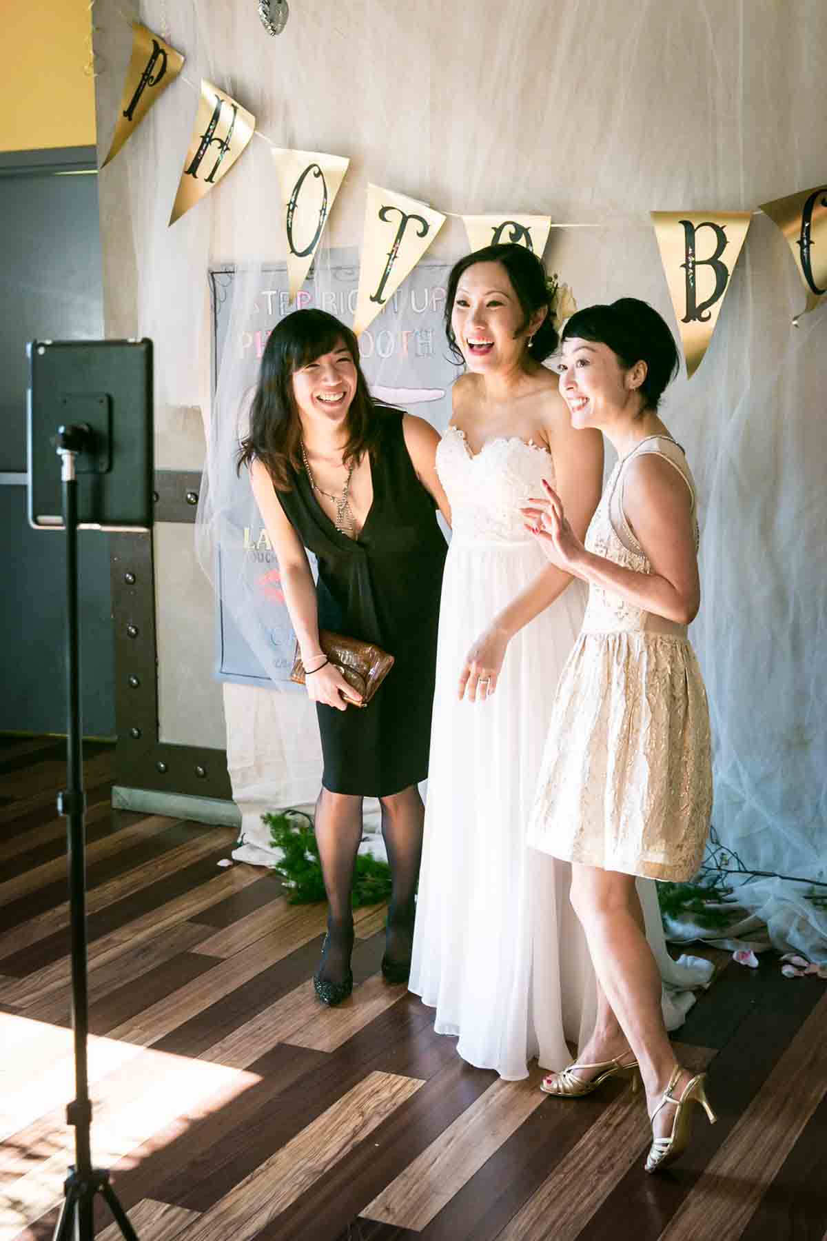 Bride and two female guests having fun in front of photo booth camera