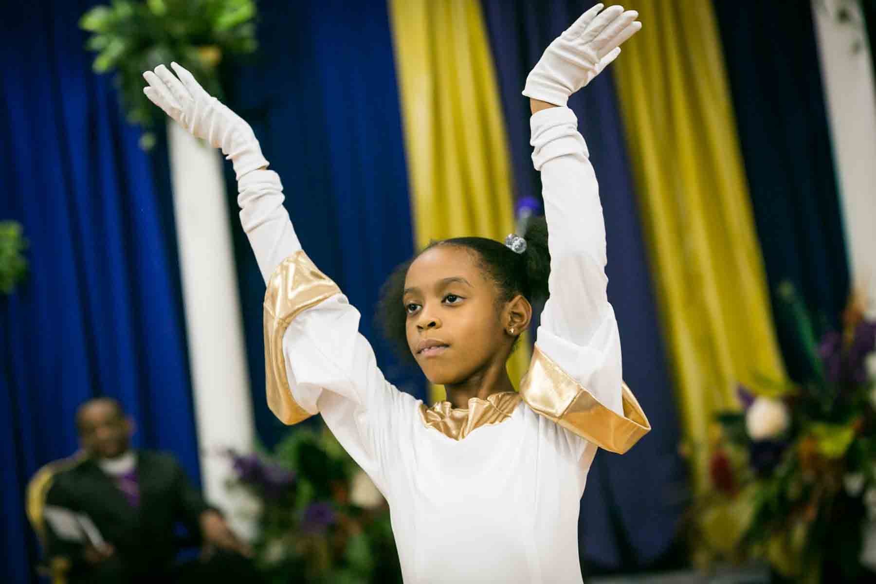 Little dancer wearing white outfit and long white gloves with hands in the air