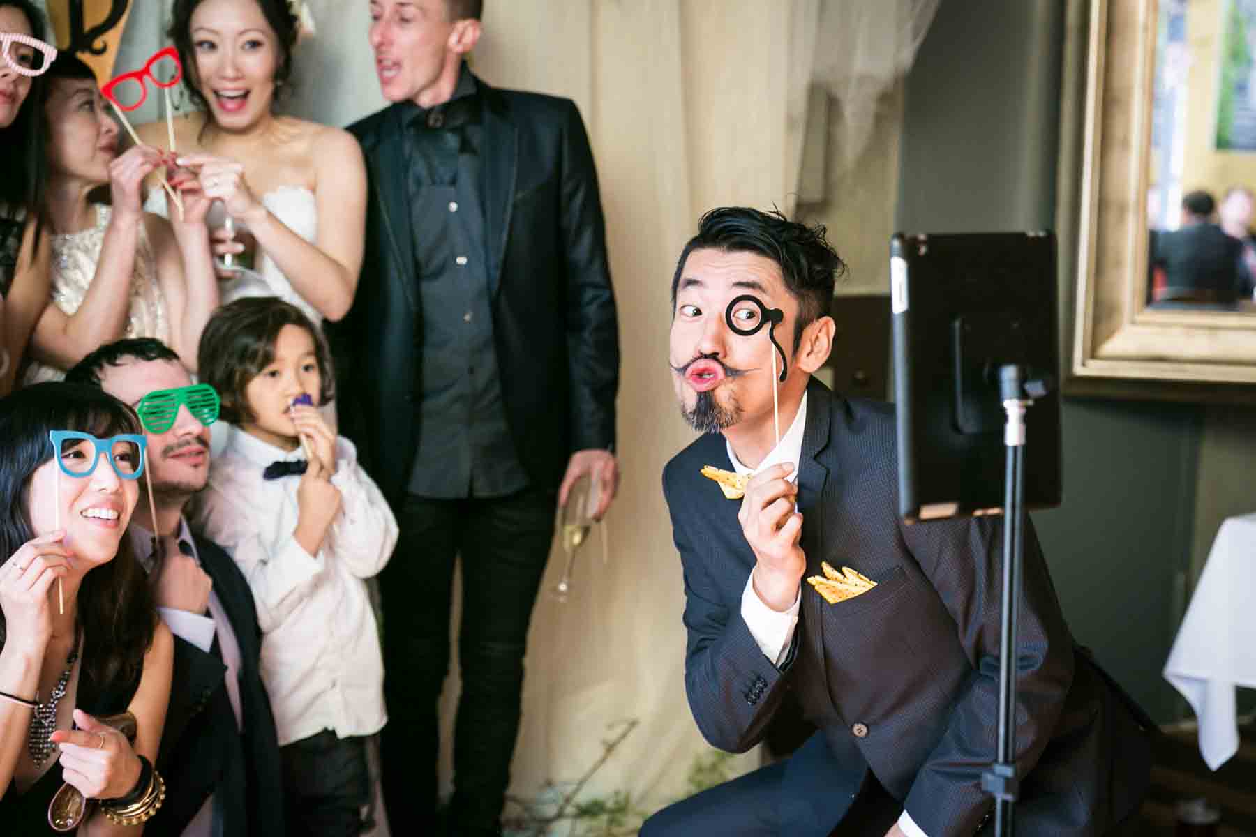 Man playing with guests in front of photo booth camera for an article on the best wedding jobs for family and friends