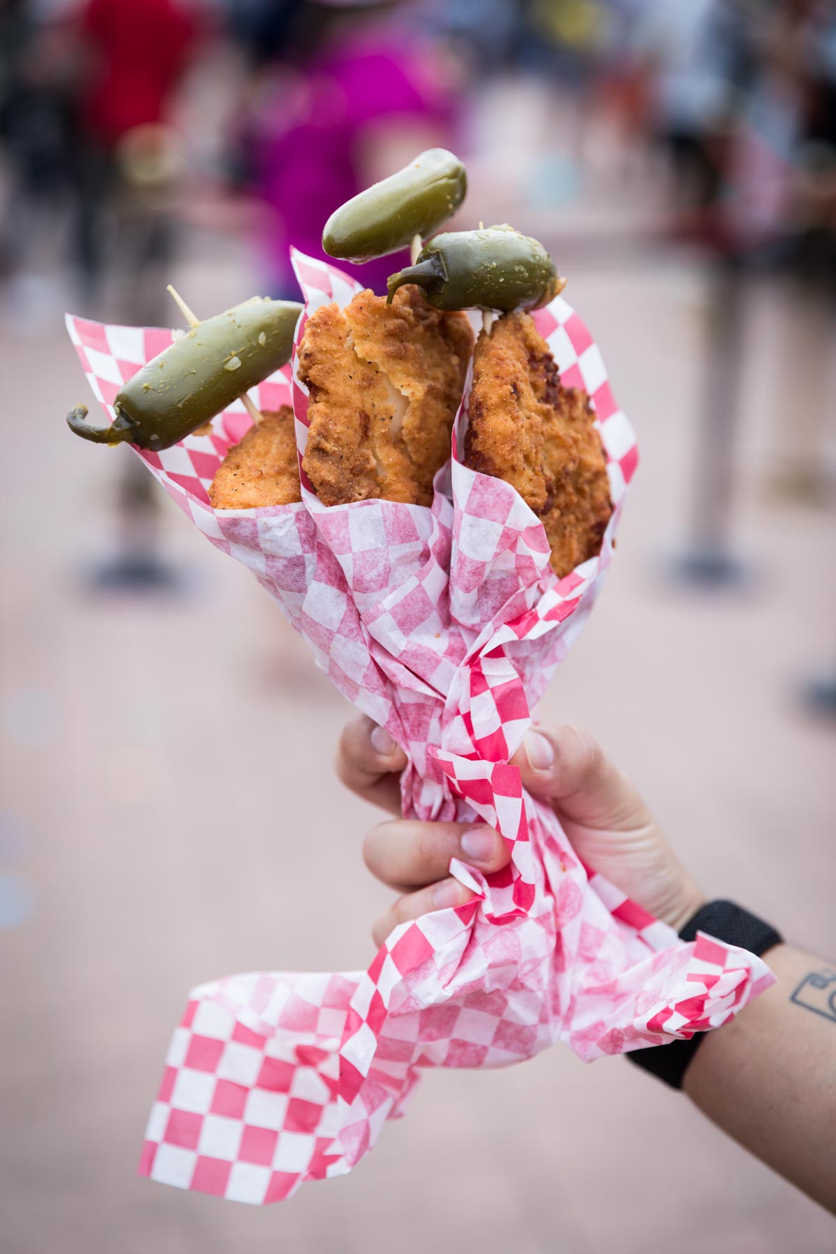Hand holding three pieces of chicken on a stick with jalapenos