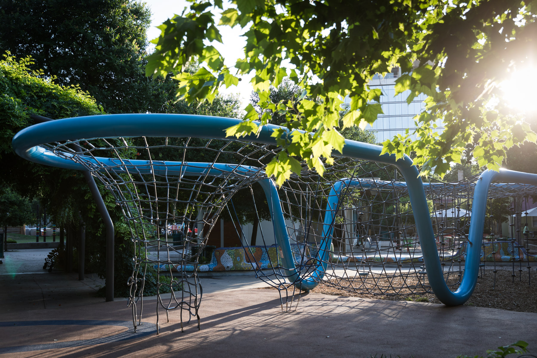 Playground sculpture with net and blue tubing with trees in Yanaguana Garden in Hemisfair for an article on the perfect downtown San Antonio family portrait itinerary