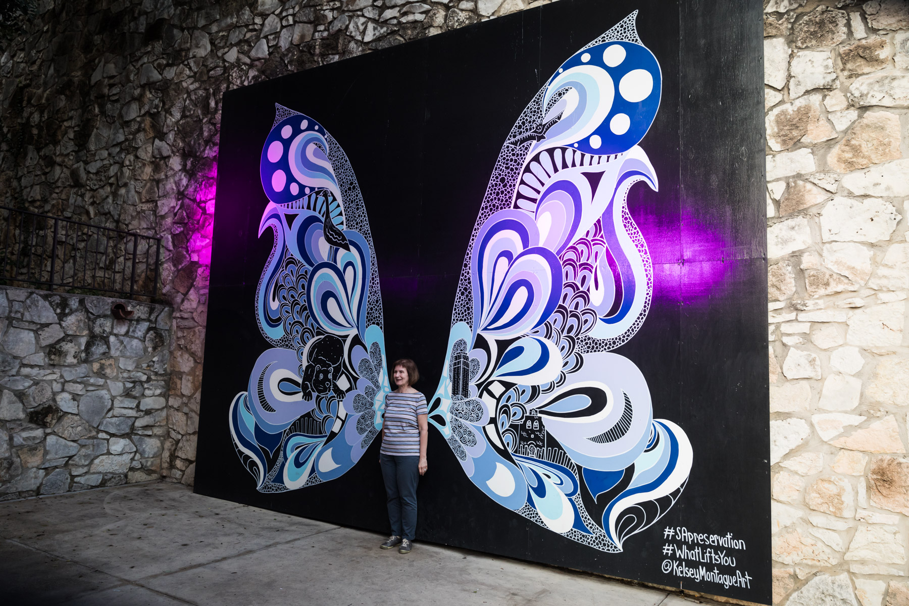 Woman standing in front of public mural of decorative butterfly wings on stone wall for an article on the perfect downtown San Antonio family portrait itinerary