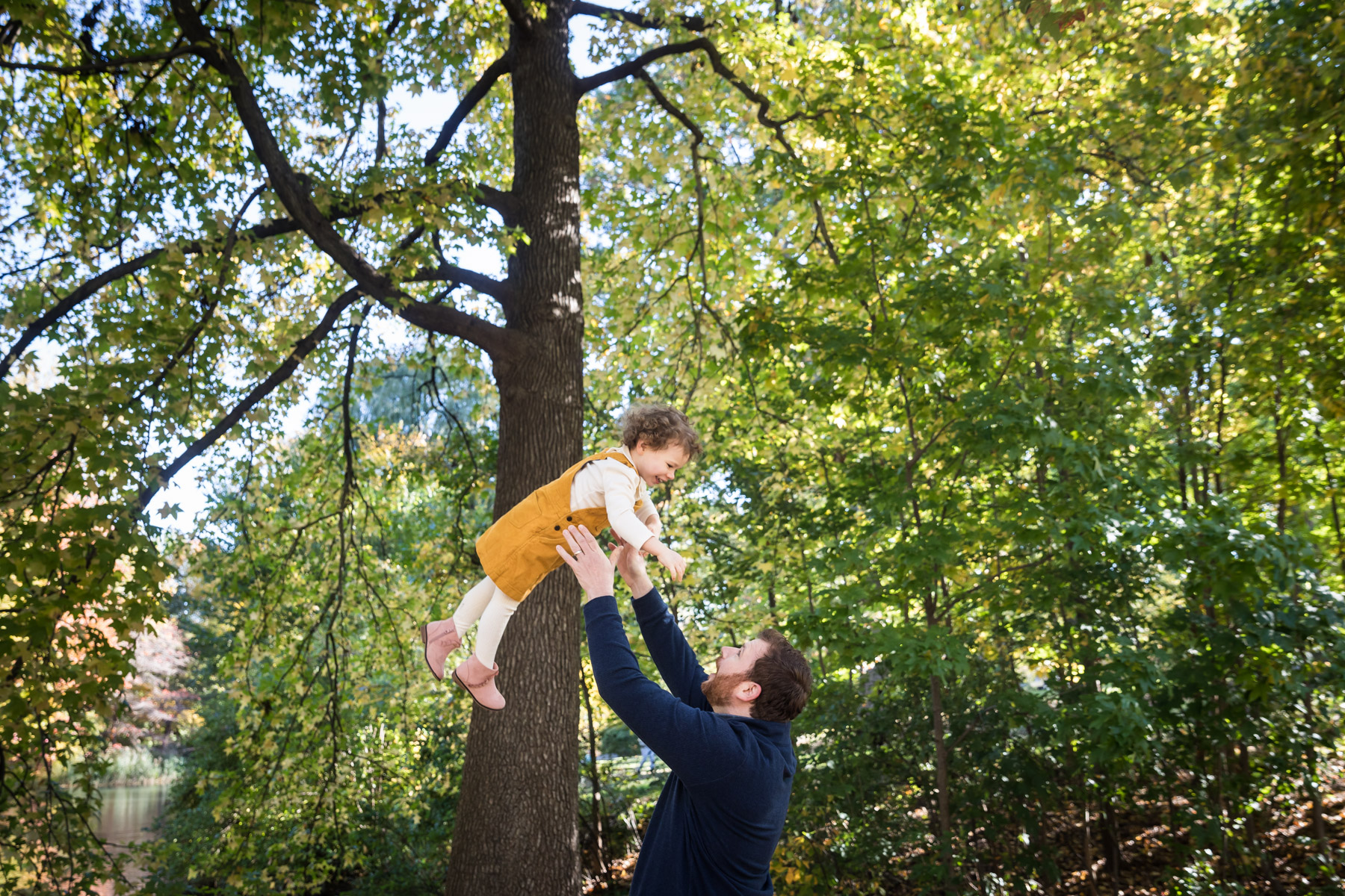 Father throwing little girl in the air with trees in background for an article on the perfect downtown San Antonio family portrait itinerary