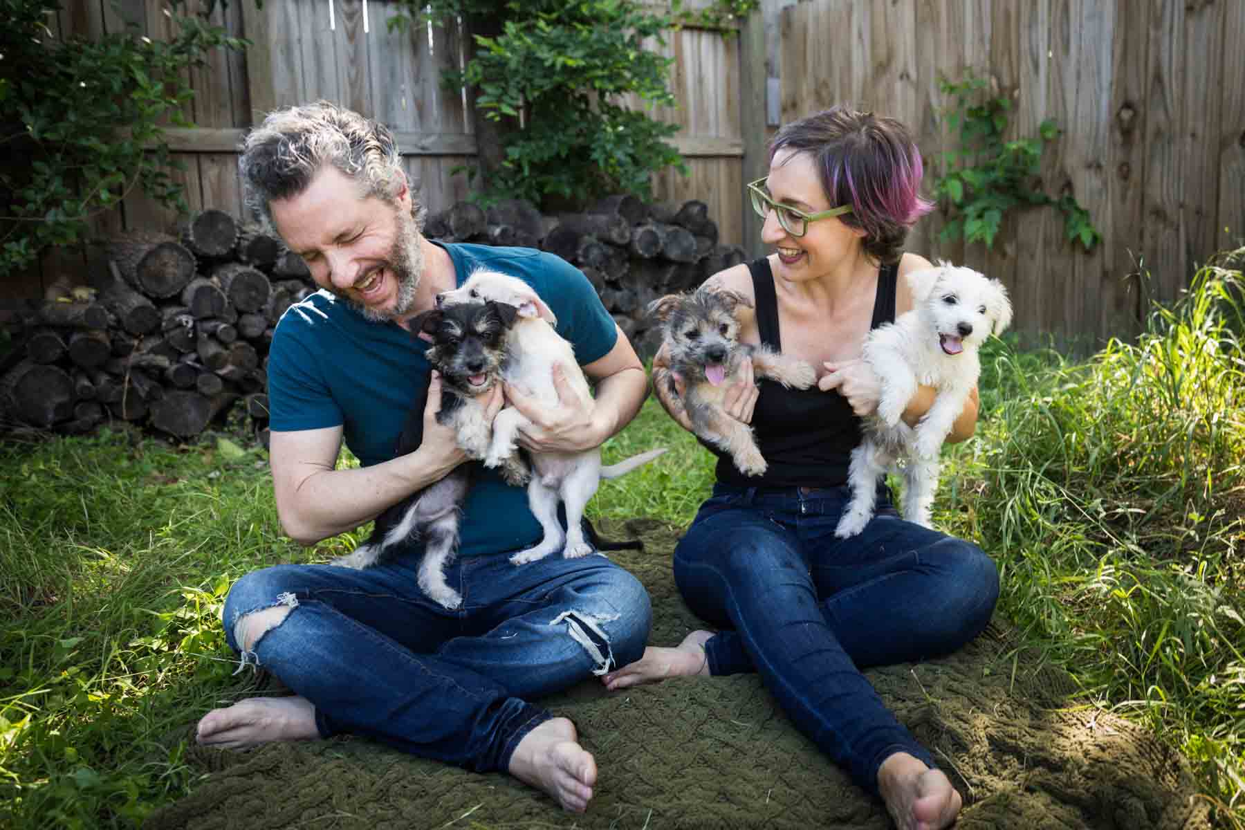 Man and woman sitting cross-legged on ground holding puppies for an article on pet photo tips