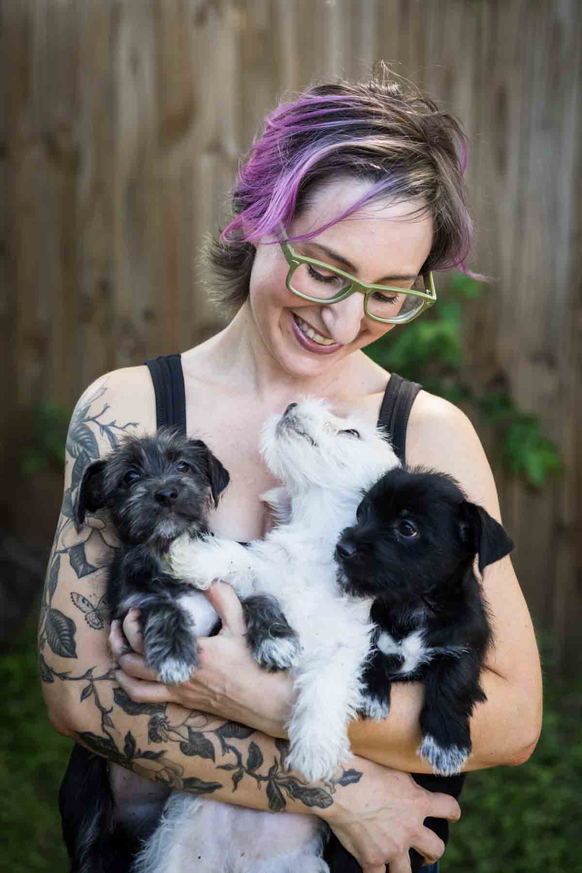 Woman with purple hair and glasses holding three puppies for an article on pet photo tips