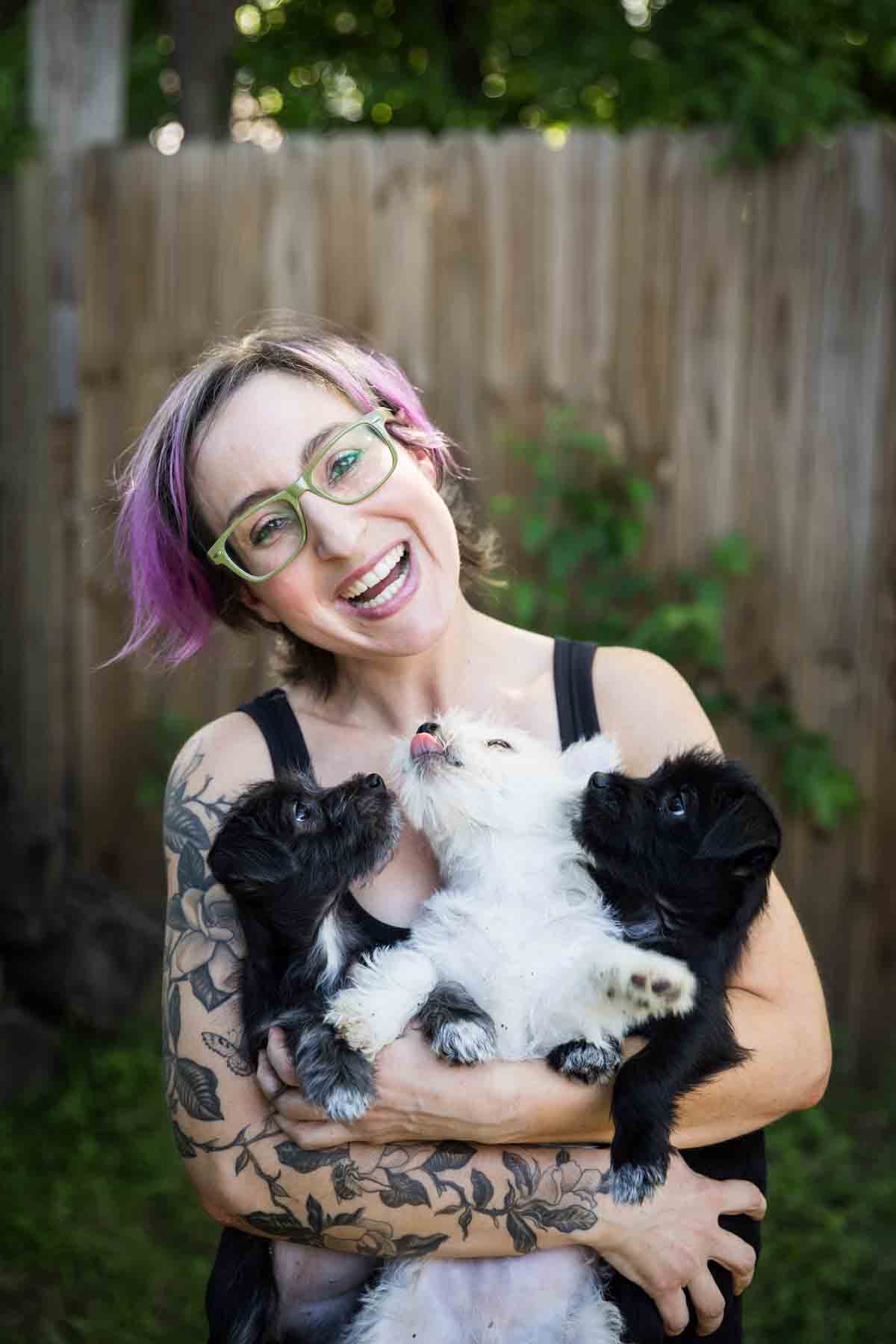 Woman with purple hair and glasses holding three puppies for an article on pet photo tips