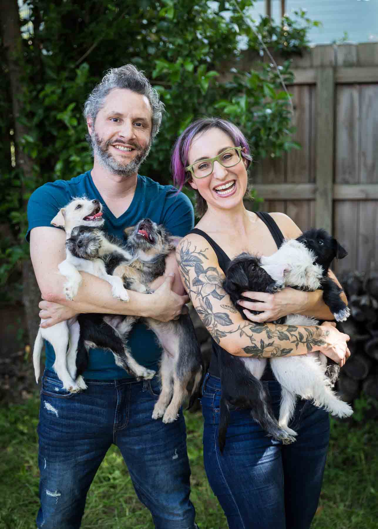 Man and woman holding puppies in their arms in front of wooden fence for an article on pet photo tips