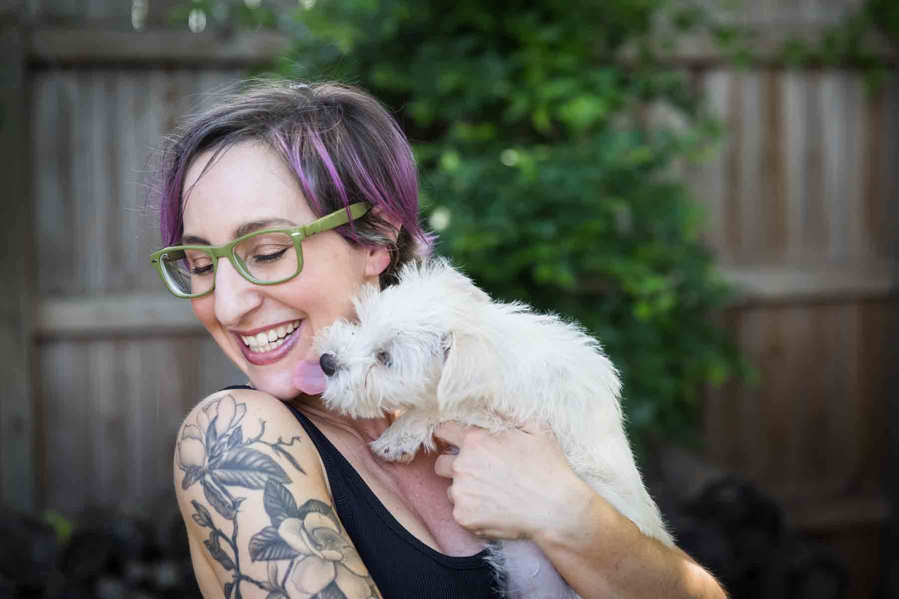 Woman with purple hair and glasses holding a white puppy for an article on pet photo tips