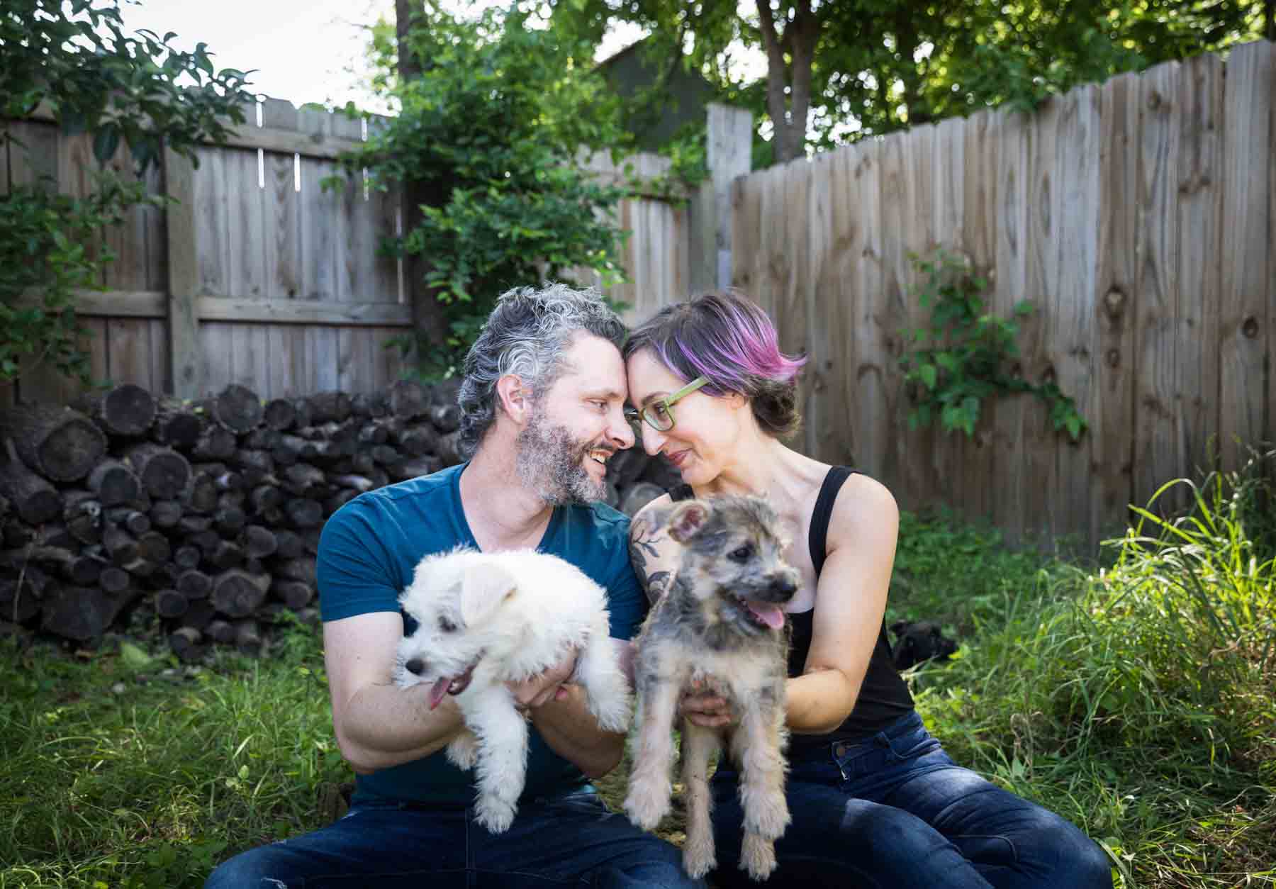 Couple pressing foreheads together while sitting on ground holding puppies for an article on pet photo tips