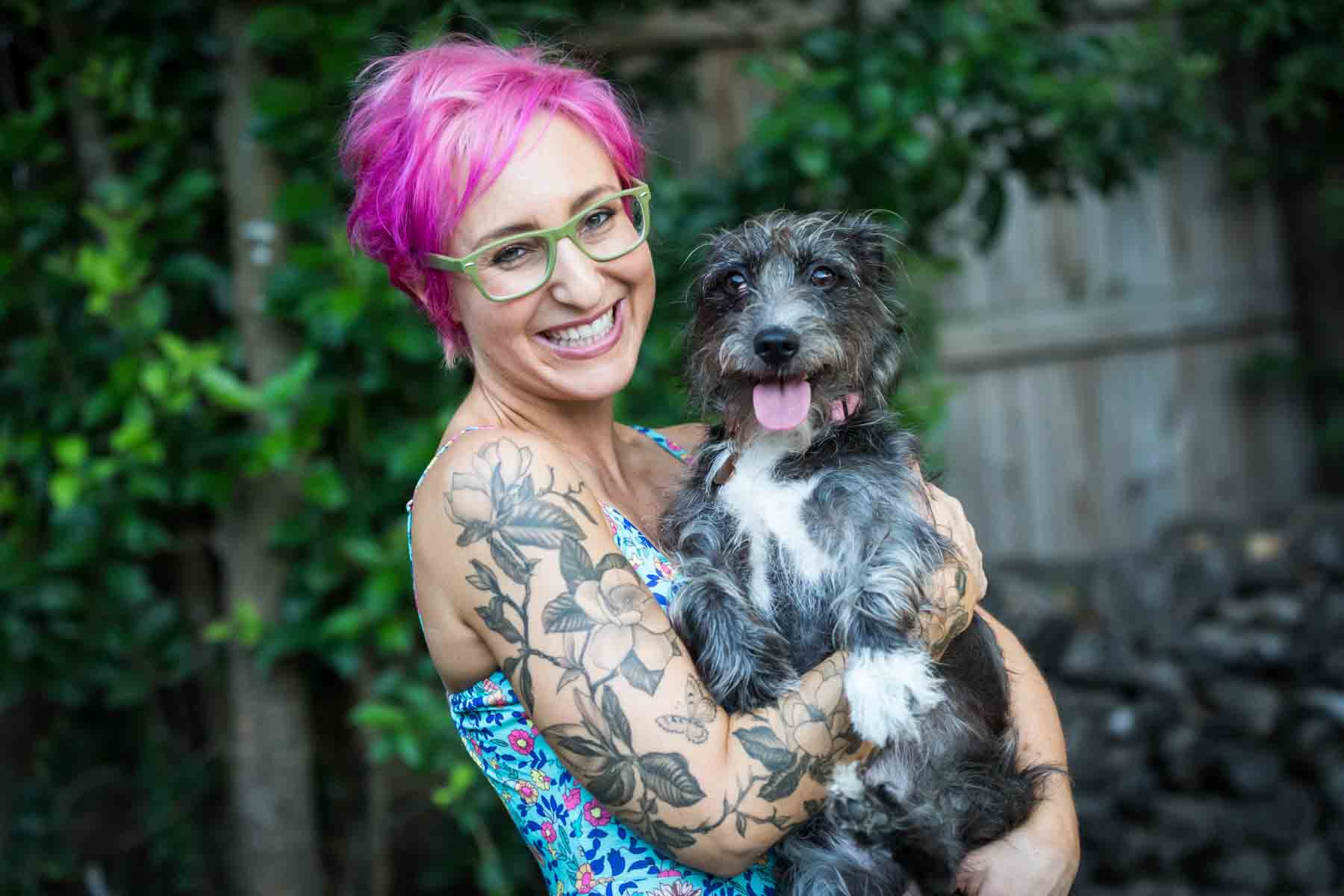 Woman with pink hair and glasses holding a grey dog for an article on pet photo tips