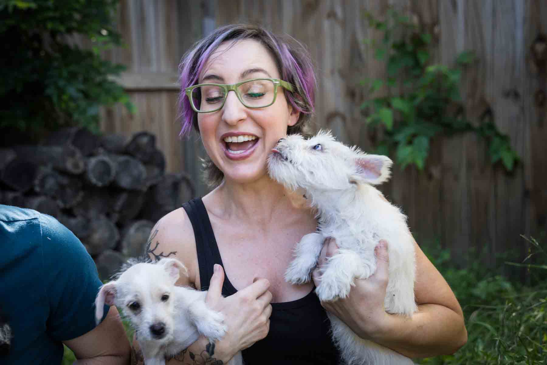 Woman with purple hair and glasses holding two white puppies for an article on pet photo tips