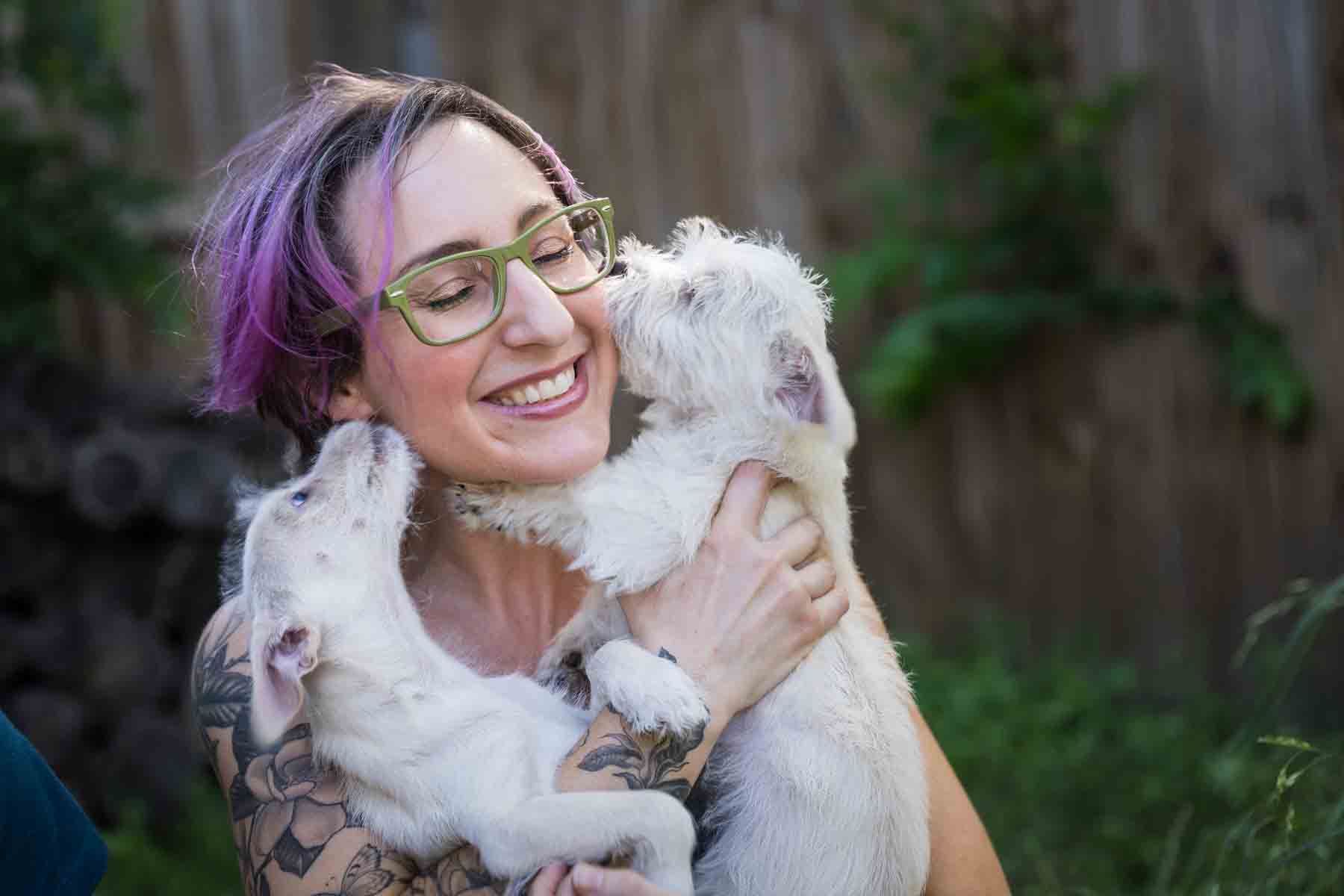 Woman with purple hair and glasses holding two puppies for an article on pet photo tips