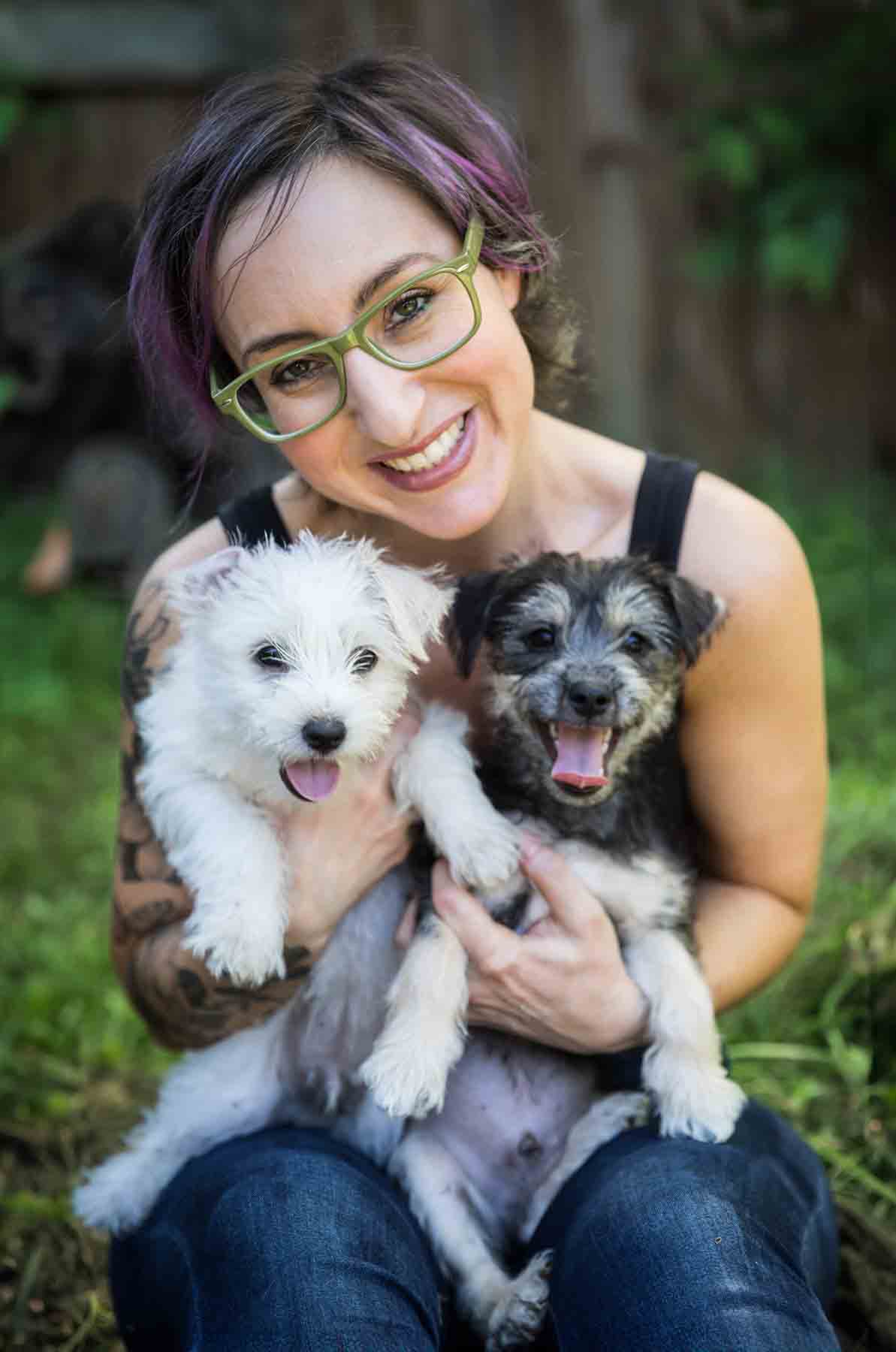 Woman with purple hair and glasses holding two puppies for an article on pet photo tips