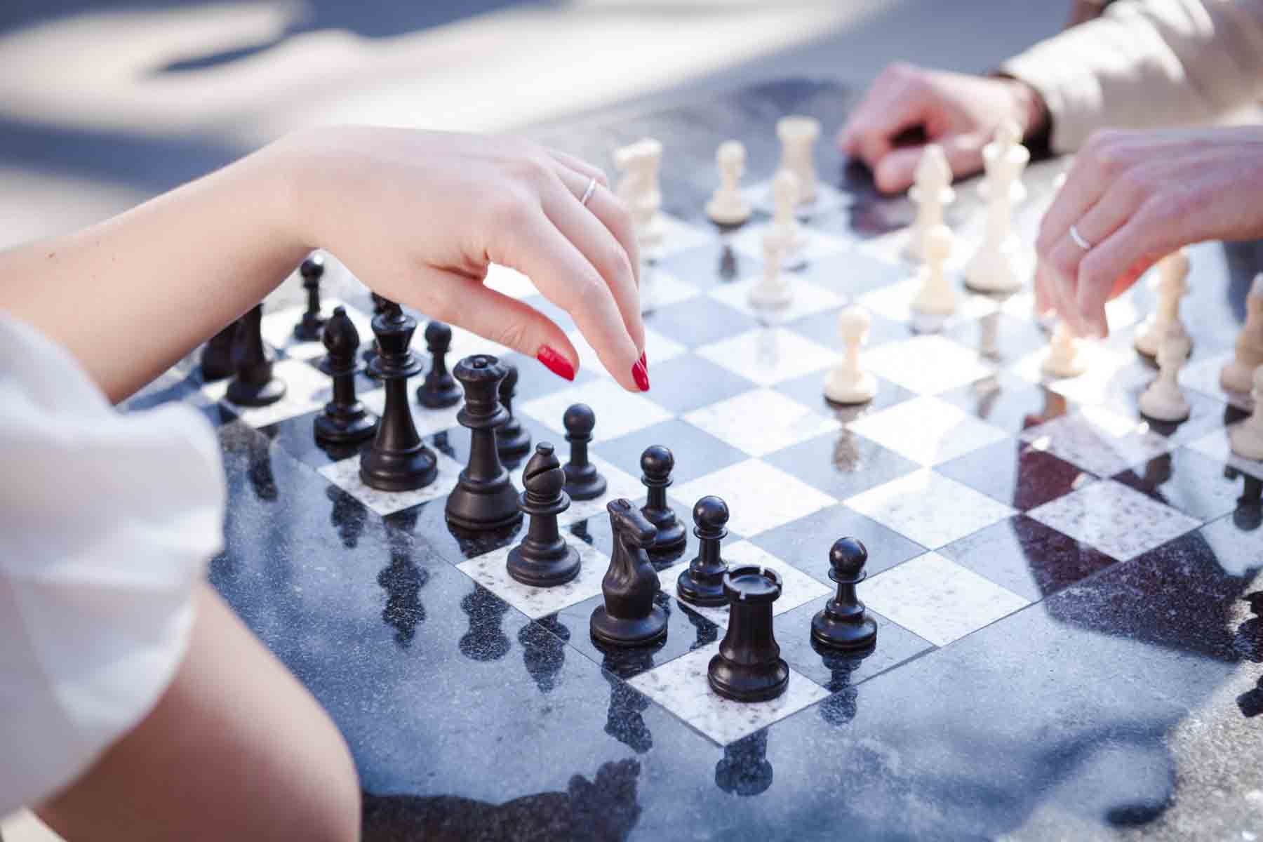 Close up of woman's hand wearing wedding ring above chess board for an article entitled, ‘Are Couples Still Getting Married?’