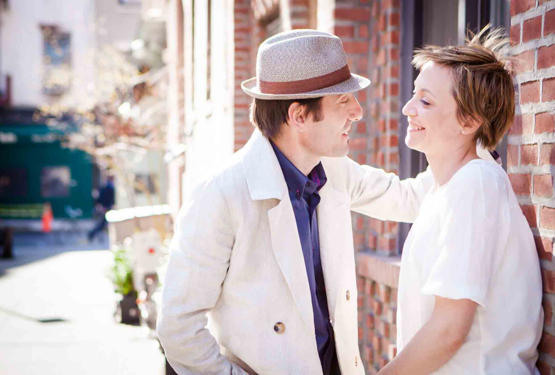 Man looking at woman with short hair against brick wall for an article entitled, ‘Are Couples Still Getting Married?’