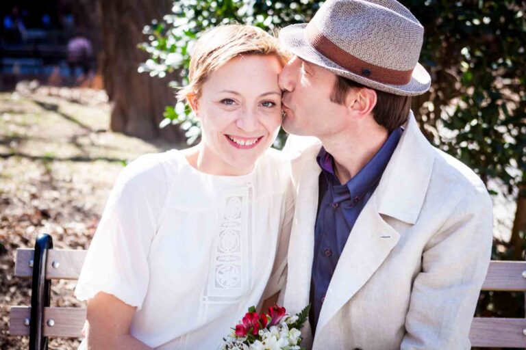 Man wearing fedora kissing woman with short hair on the side of face for an article entitled, ‘Are Couples Still Getting Married?’