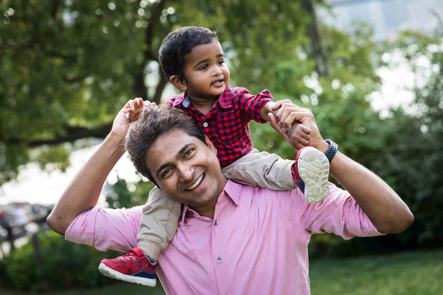 Indian American father wearing pink shirt holding little boy wearing red checked shirt on his shoulders for an article on daddy and me photo shoot ideas