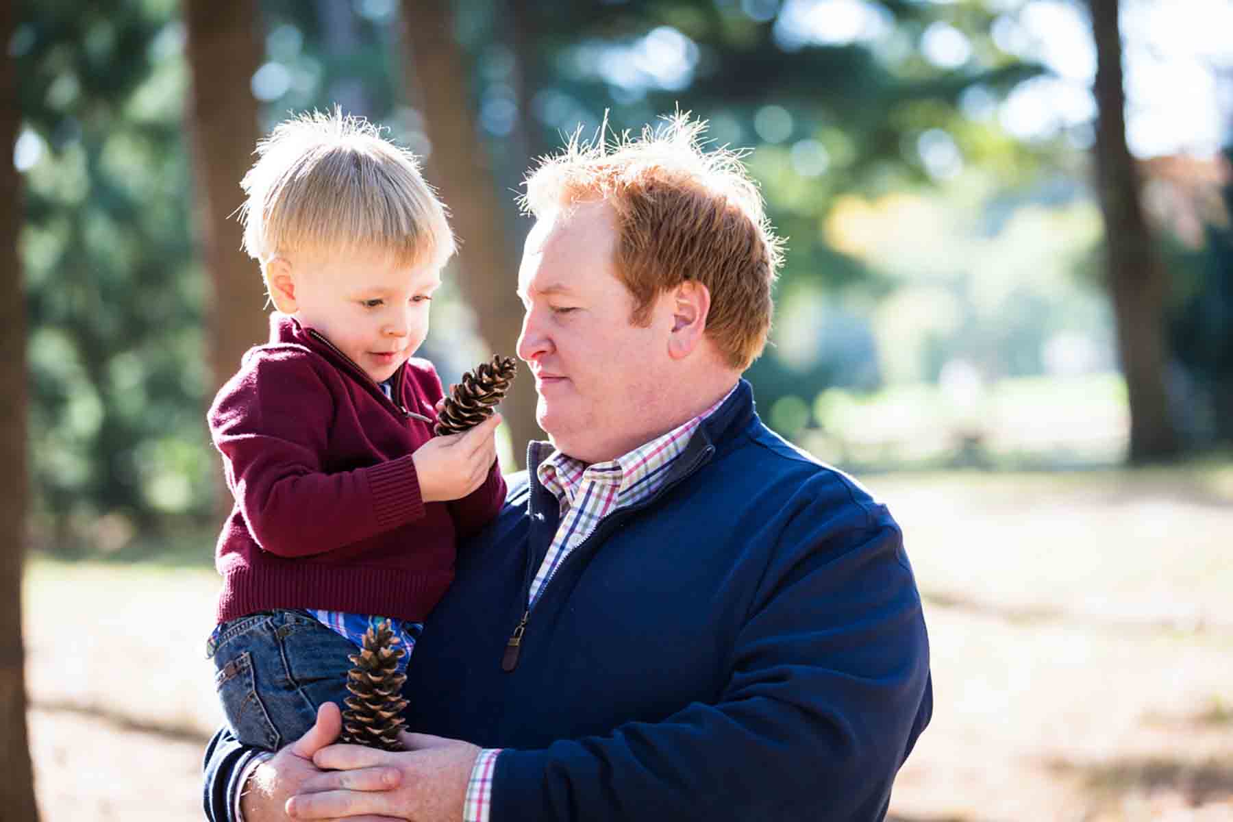 Father holding little boy in his arms studying pine cones for an article on daddy and me photo shoot ideas